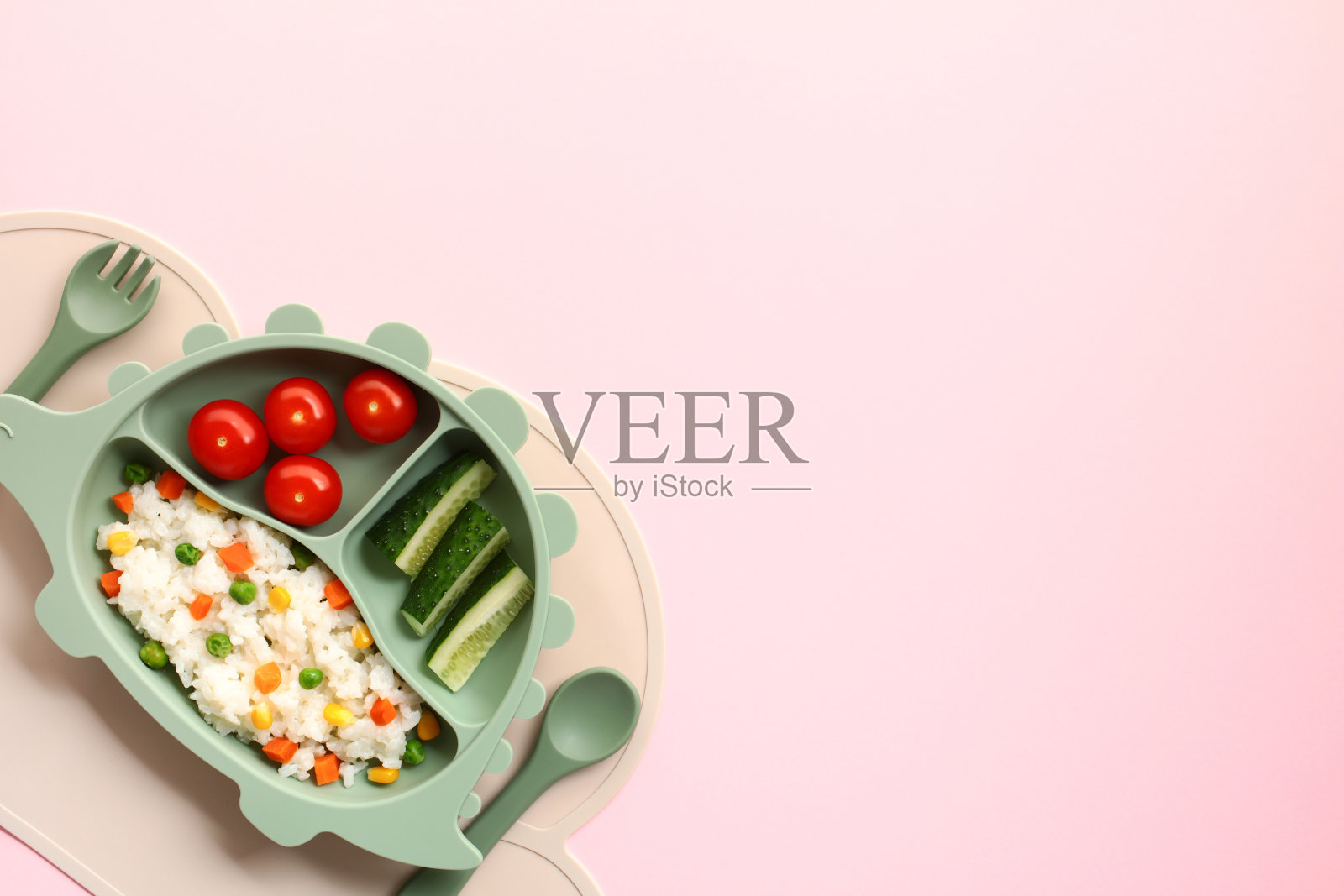 带隔板的幼儿餐盘，盛满米饭、西红柿和黄瓜，背景为粉色照片摄影图片