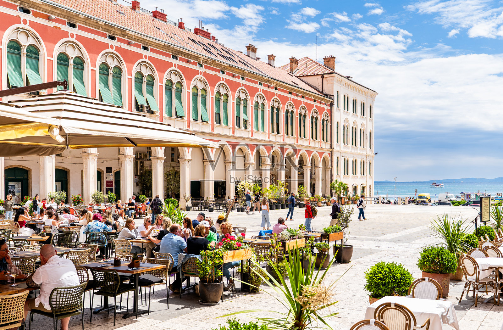 人群在斯普利特老城的共和国广场上坐着和走动,周围是排成行的石拱门。照片摄影图片