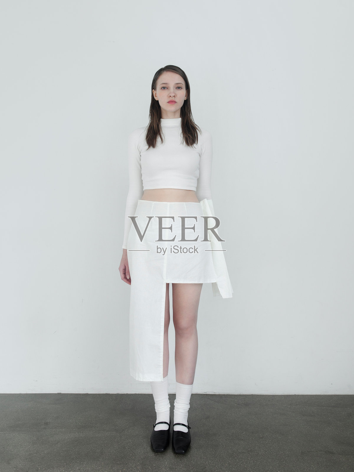 美丽的年轻女性全身肖像时尚模特，穿着韩国风格设计师服装，整体白色造型，身材高挑纤细，长袖上衣，不对称裙子，高筒袜，黑色平底鞋，迷人的肖像，棕色头发，大蓝眼睛。照片摄影图片