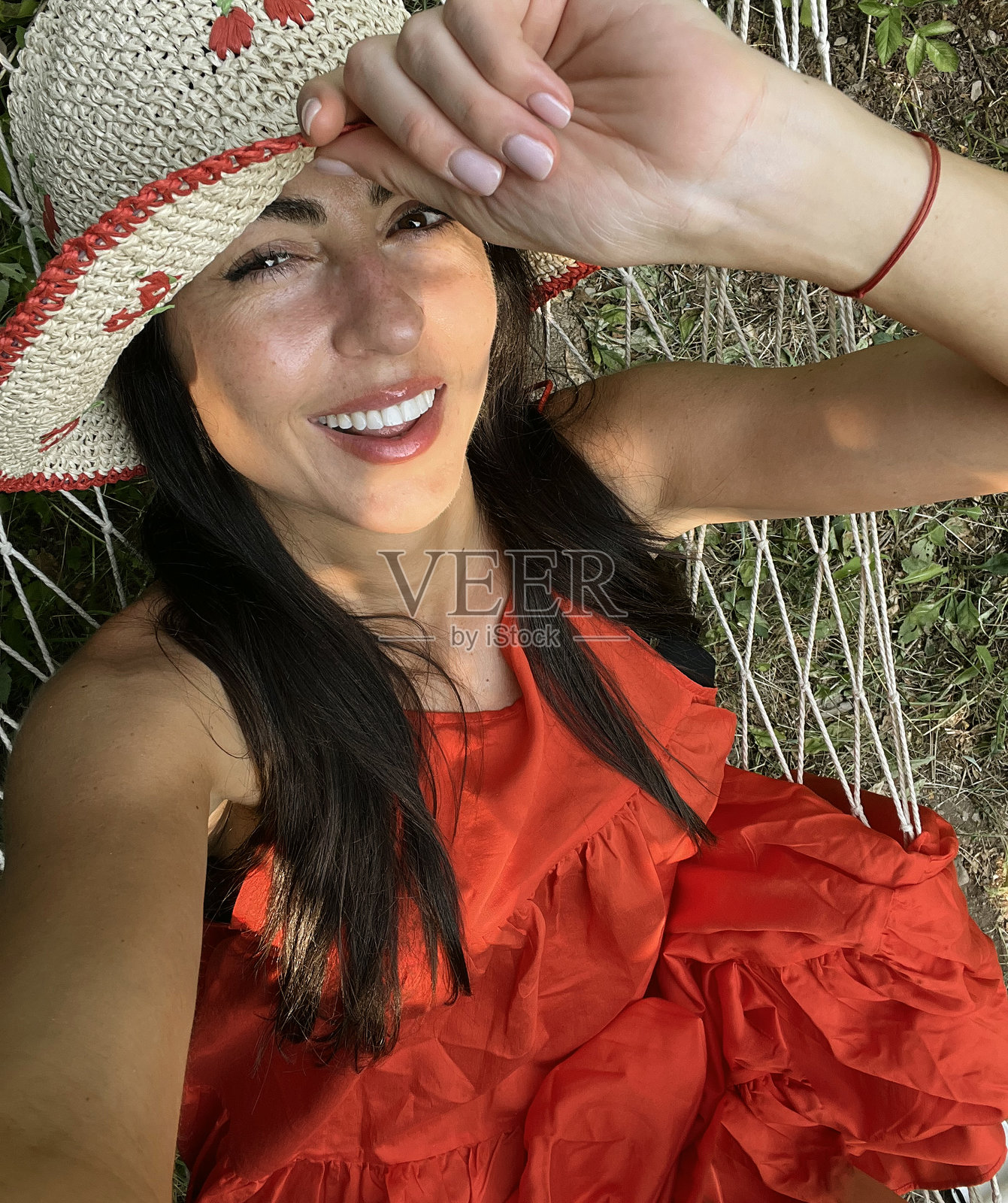戴着帽子和红色连衣裙的女人在吊床上放松照片摄影图片