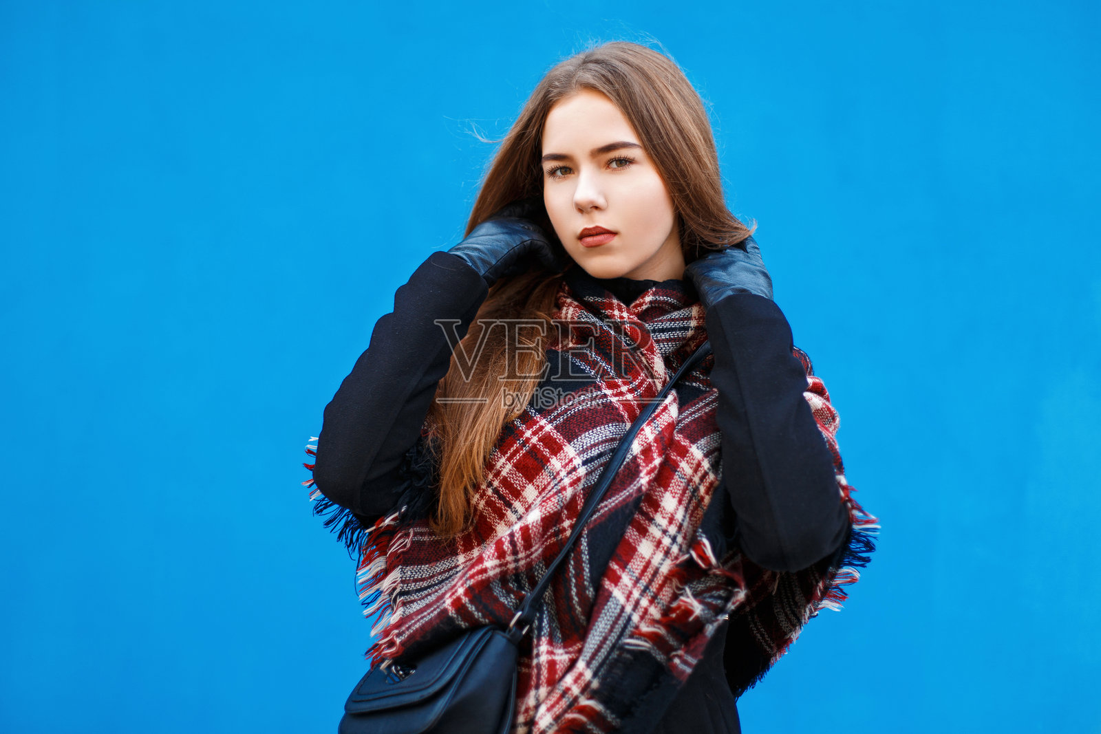 身穿围巾和外套的美丽女性在明亮的蓝色墙壁旁摆姿势照片摄影图片