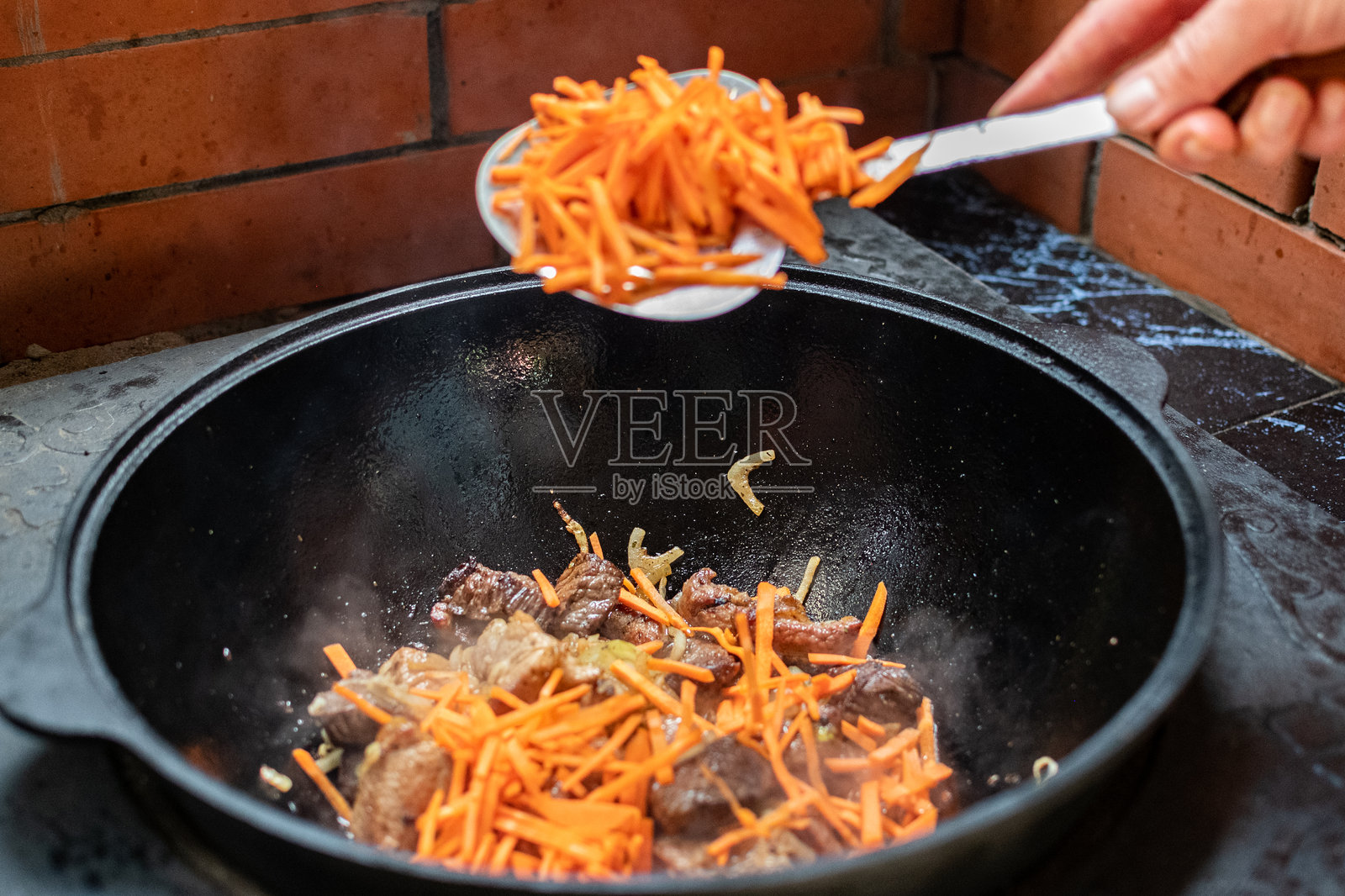 羊肉块与洋葱在火上热油中炸制。传统米饭的准备。用铸铁锅烹饪米饭。照片摄影图片