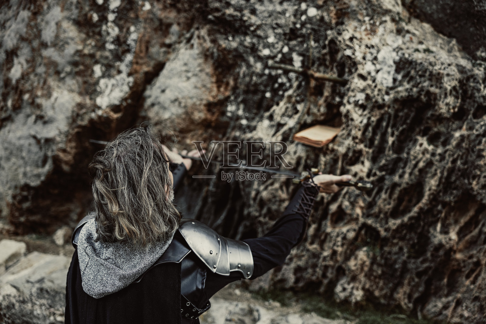 黑色盔甲骑士背影举剑，前方模糊的十字架和书本照片摄影图片