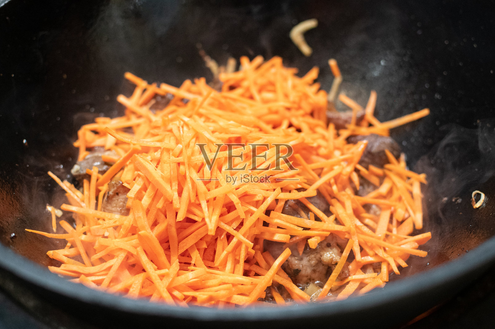 羊肉块与胡萝卜和洋葱在火上热油中炸制。传统米饭的准备。用铸铁锅烹饪米饭。照片摄影图片