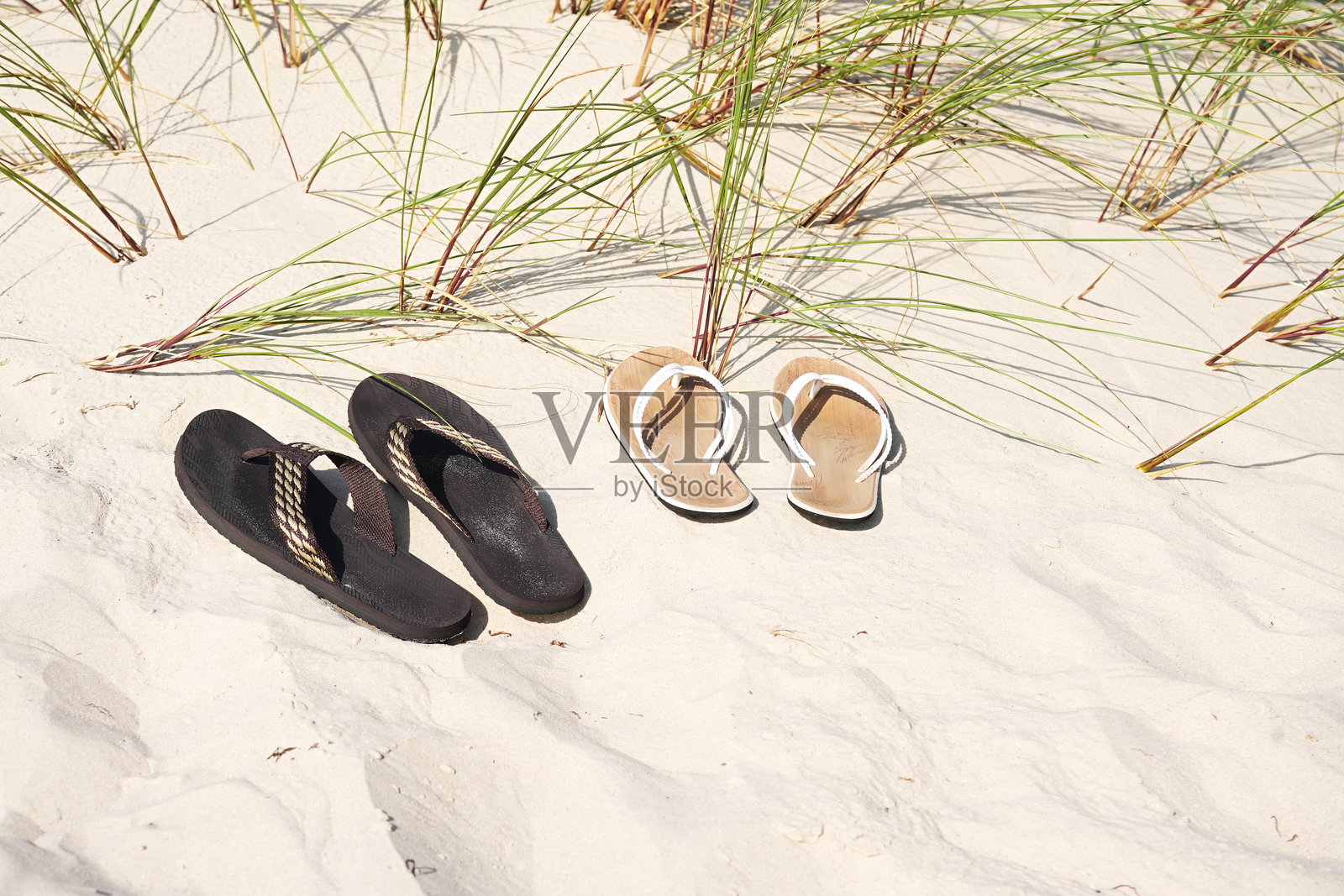 两双人字拖鞋放在沙滩上，背景有草在生长。照片摄影图片