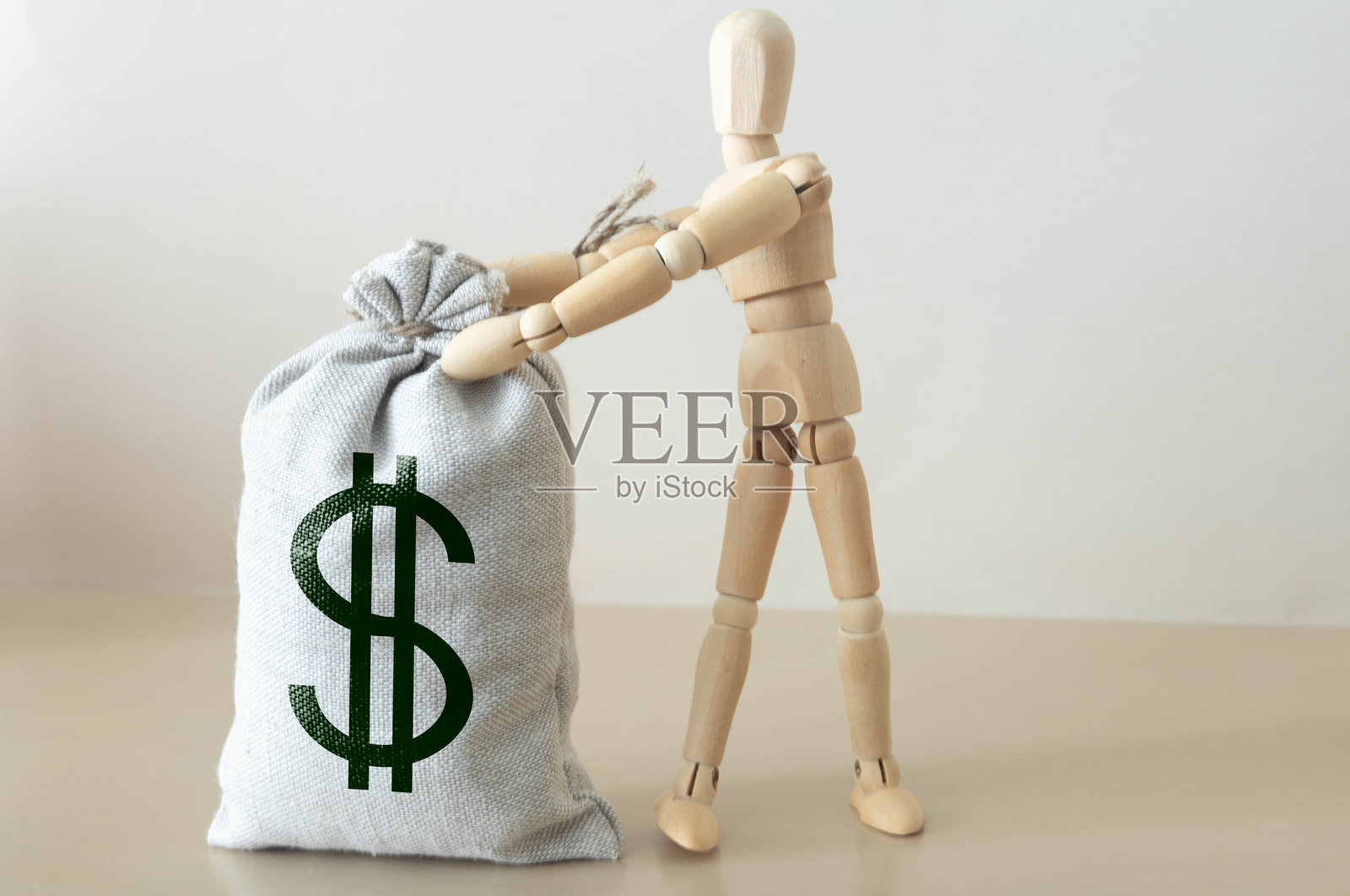 男人拉着一根绳子，后面是一个大袋子的钱，背景是灰色墙壁。照片摄影图片