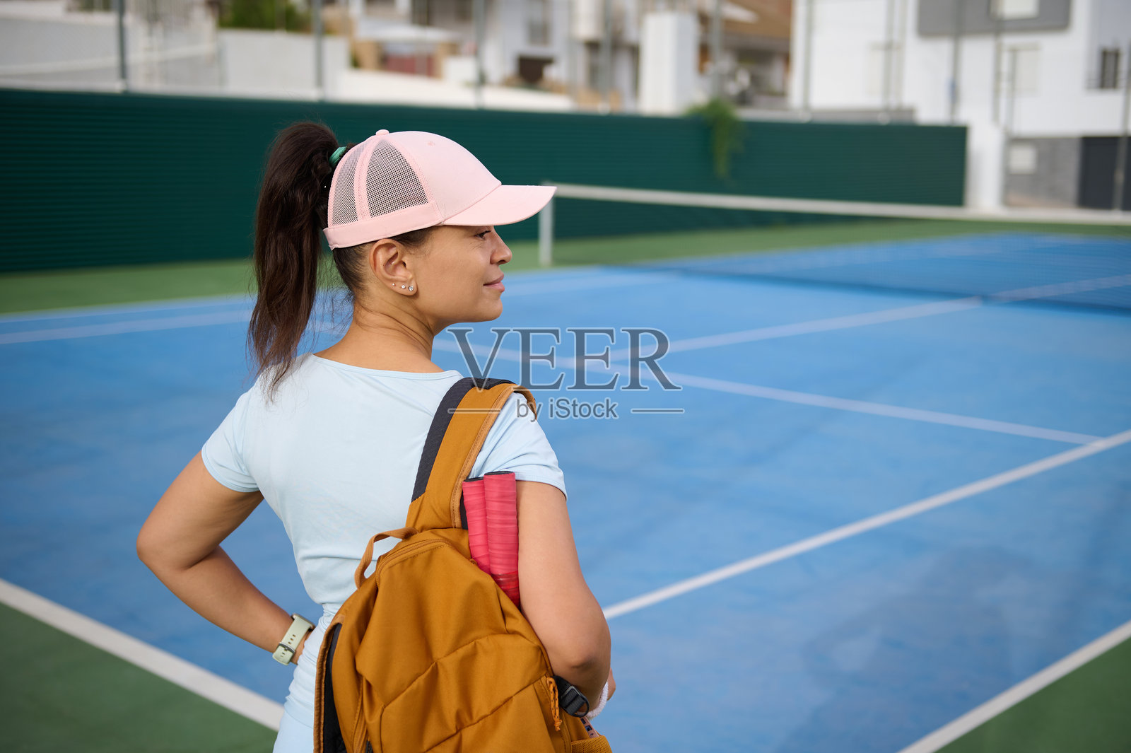 年轻女性在网球场上，背着背包，戴着帽子照片摄影图片