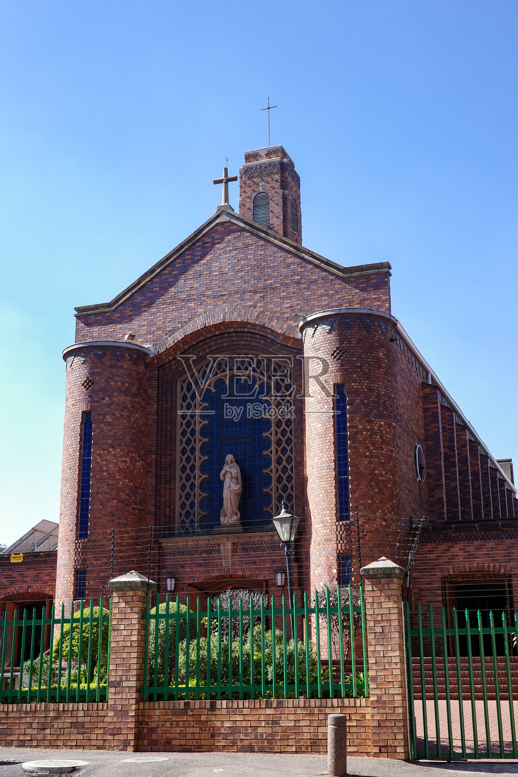 一座传统的红砖教堂外立面，配有高耸的钟楼和中央的圣母玛利亚雕像照片摄影图片