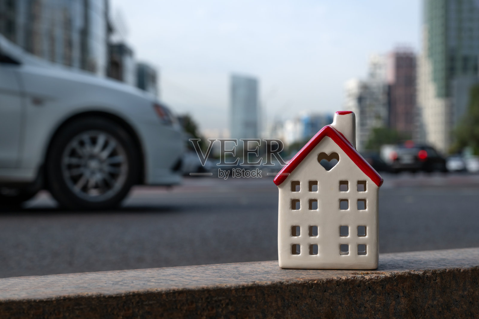 一座象征性的陶瓷房屋，背景是繁忙的城市大道，车流和新建筑交错其间。照片摄影图片