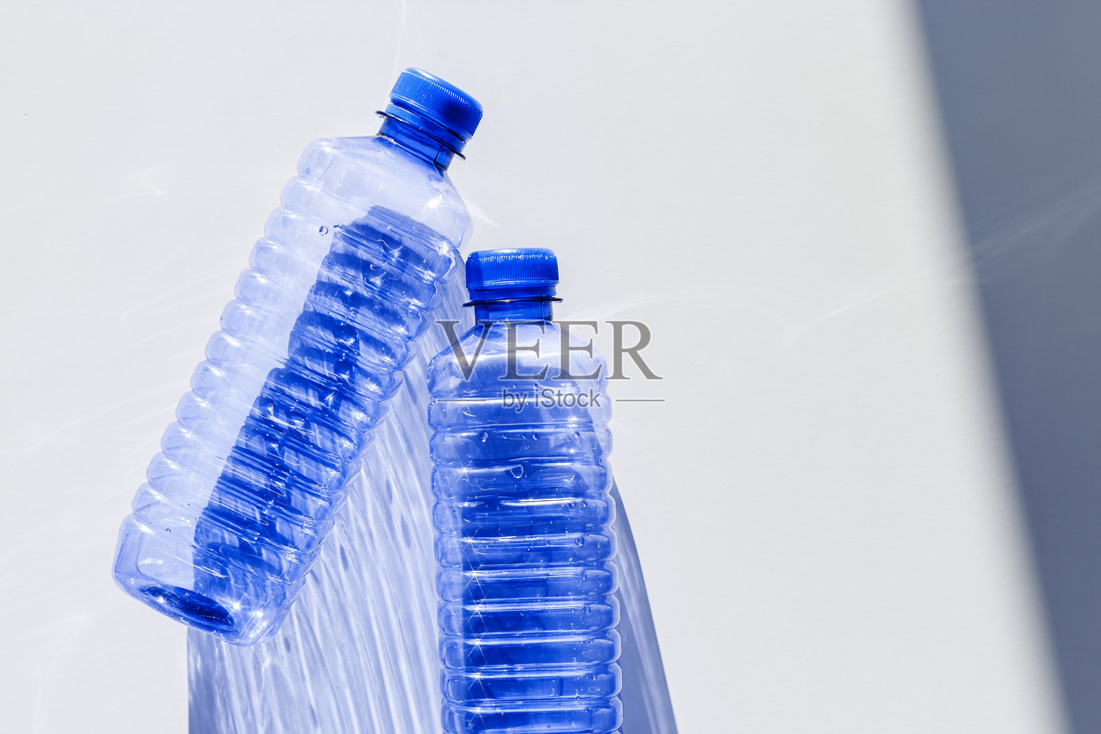 透明塑料瓶配有蓝色瓶盖，阳光在浅色背景上投下阴影。自然光下的水瓶俯视图。主题包括回收、可持续性、水资源保护、极简风格。照片摄影图片