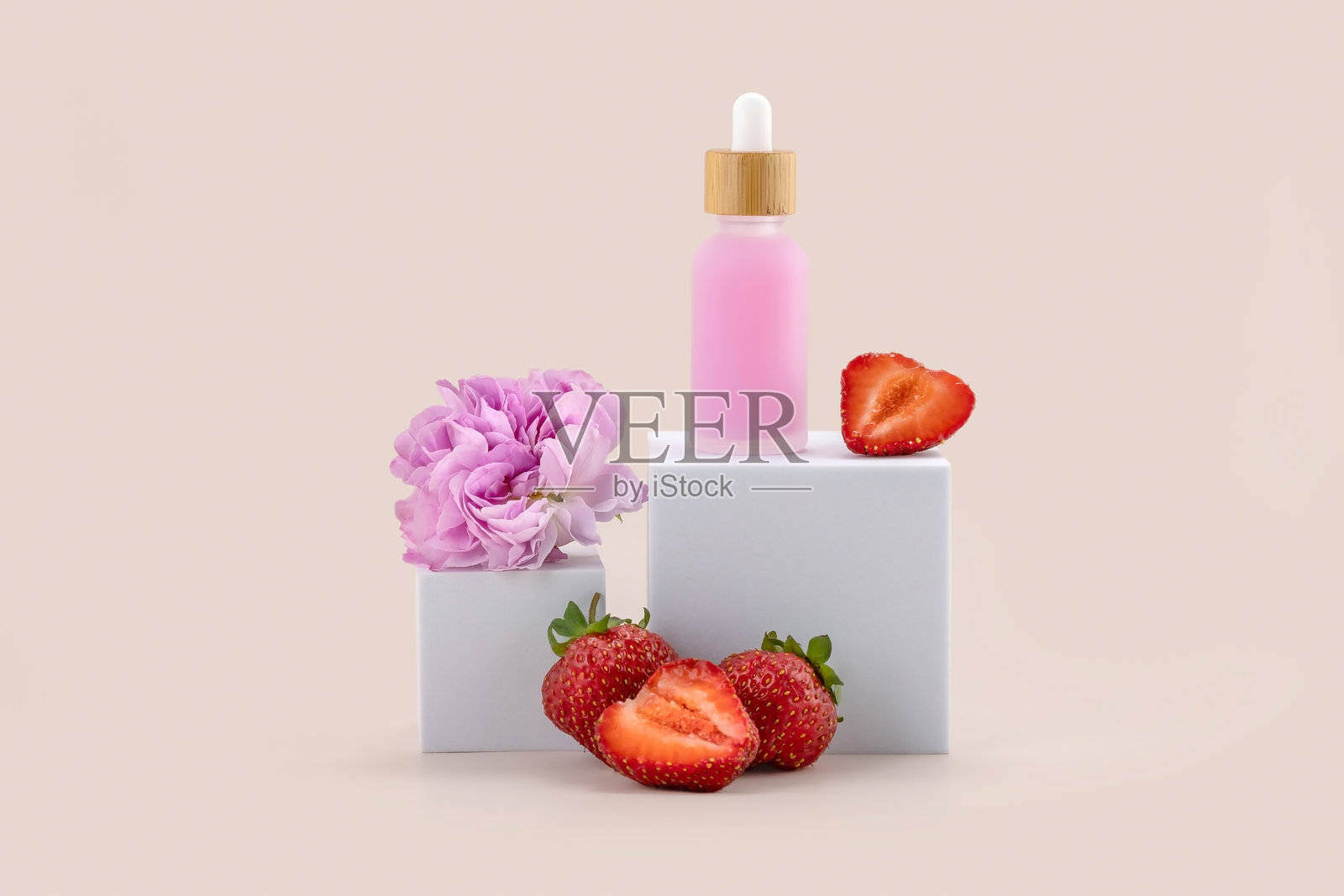 白色讲台上的滴管瓶，米色背景下有一朵玫瑰花和草莓。护肤产品的展示。照片摄影图片