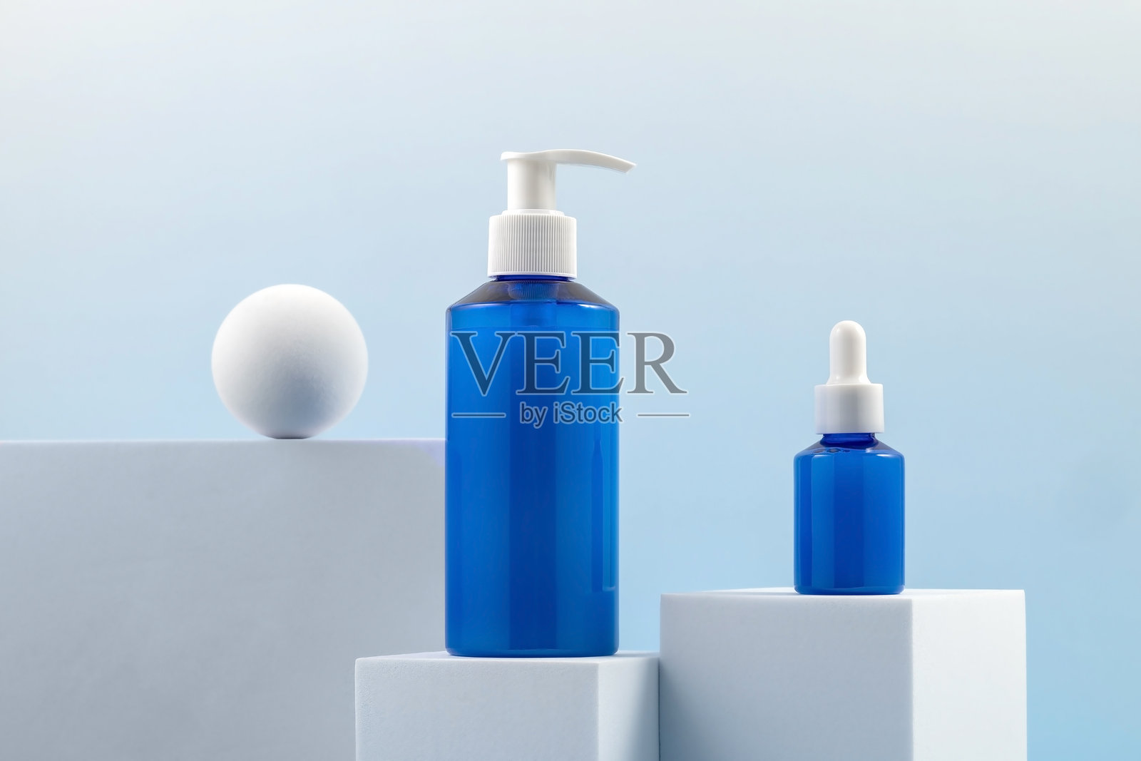 一套化妆品、面霜和精华液。白色讲台上的护肤产品容器，背景为蓝色。照片摄影图片