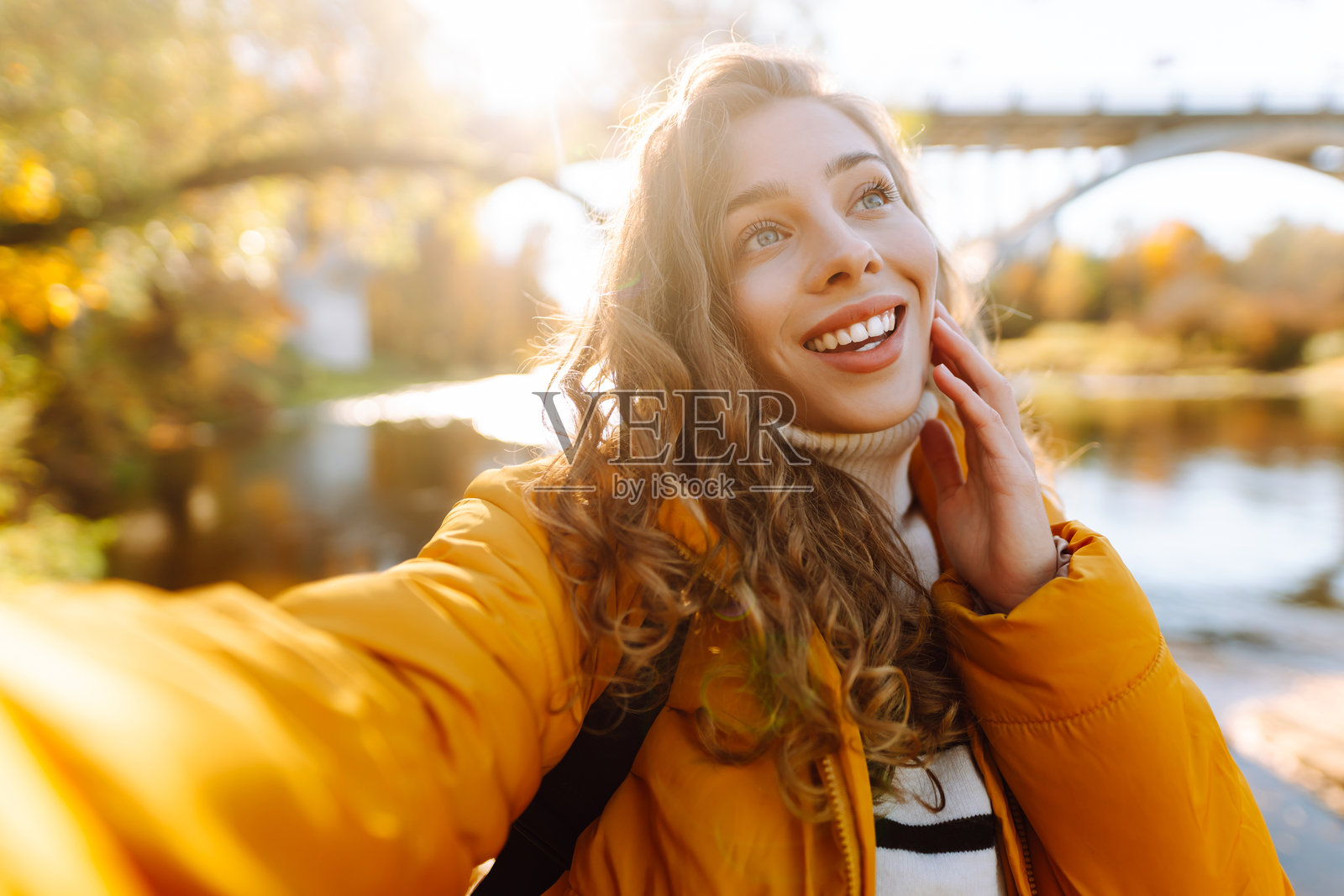快乐的女人在秋天的河岸上手握手机。照片摄影图片