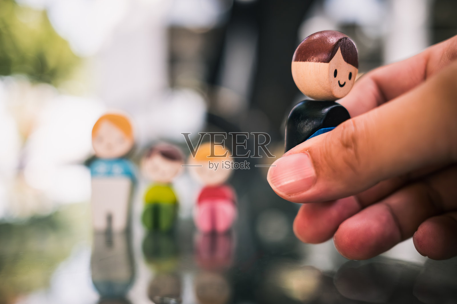 从一群木制人偶中手动挑选一个，象征着离婚、分离、破碎的家庭、情感冲突、儿童监护权、关系破裂或在父母之间的选择。照片摄影图片