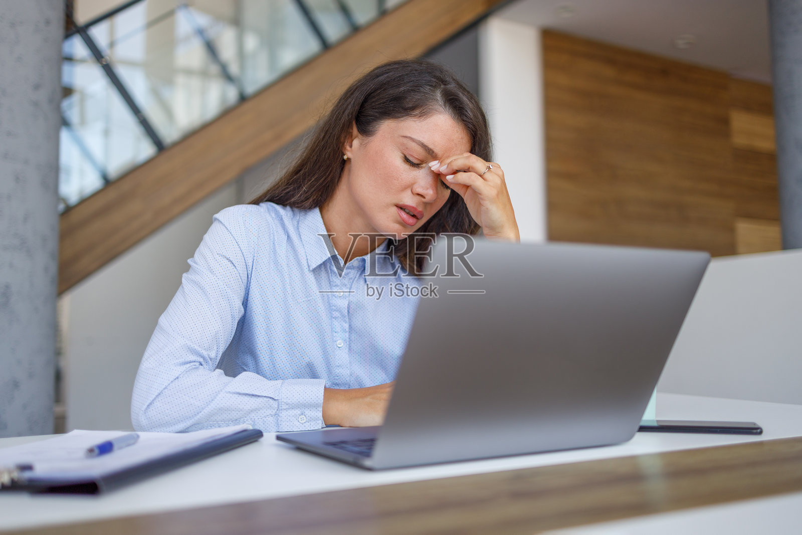 感到压力的女商人一边工作在笔记本电脑上，一边忍受头痛。照片摄影图片