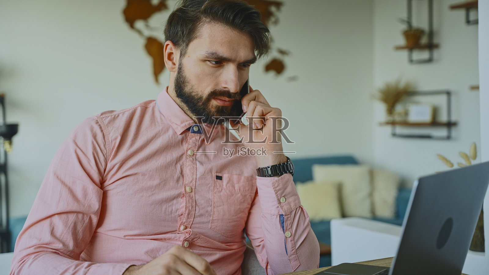 专注的商人在家办公室用智能手机通话并在笔记本电脑上工作照片摄影图片