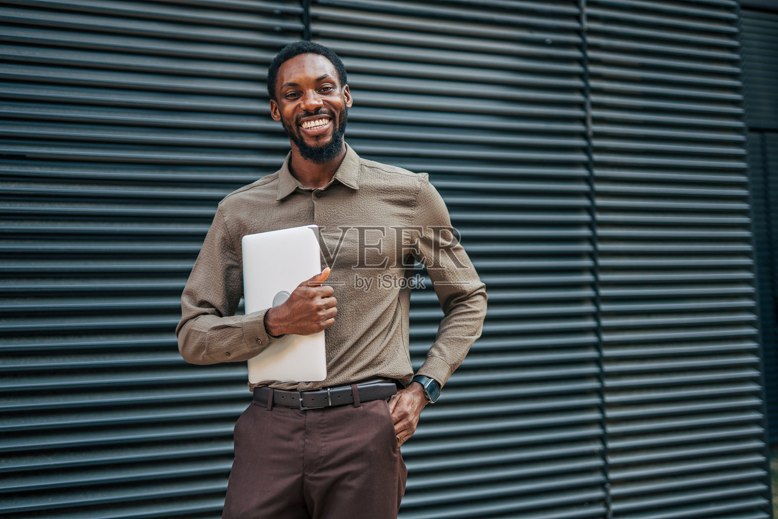 微笑的商人手持笔记本电脑，站在现代办公大楼旁照片摄影图片