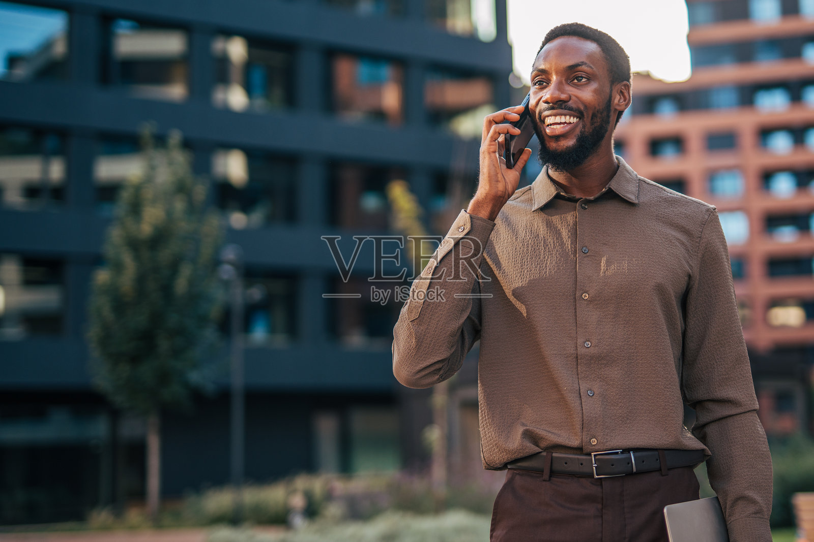 微笑的商人在办公楼外打电话照片摄影图片