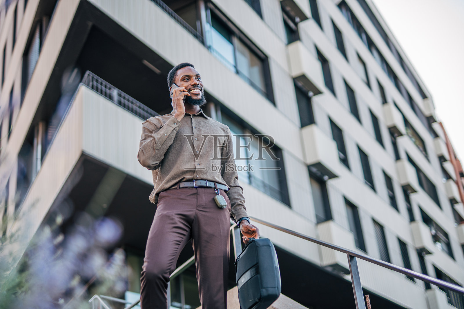商人在现代建筑前走路并打电话照片摄影图片