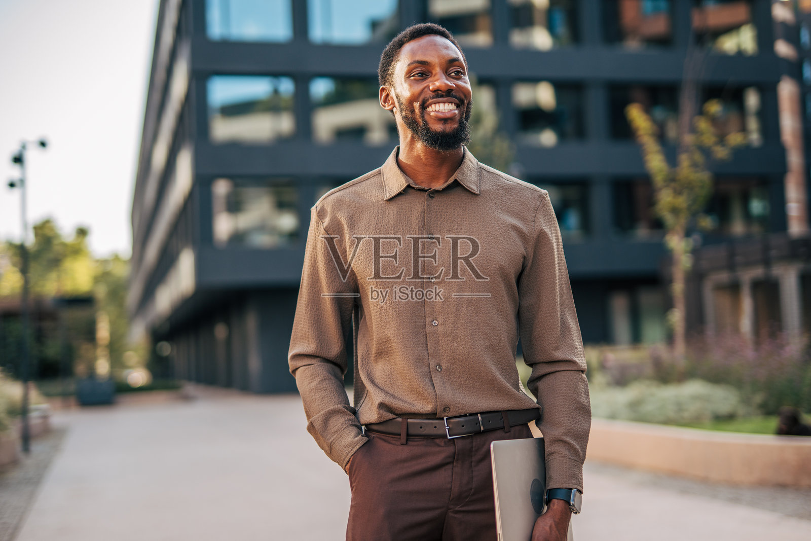 微笑的商人在办公室外走着，手里拿着笔记本电脑照片摄影图片