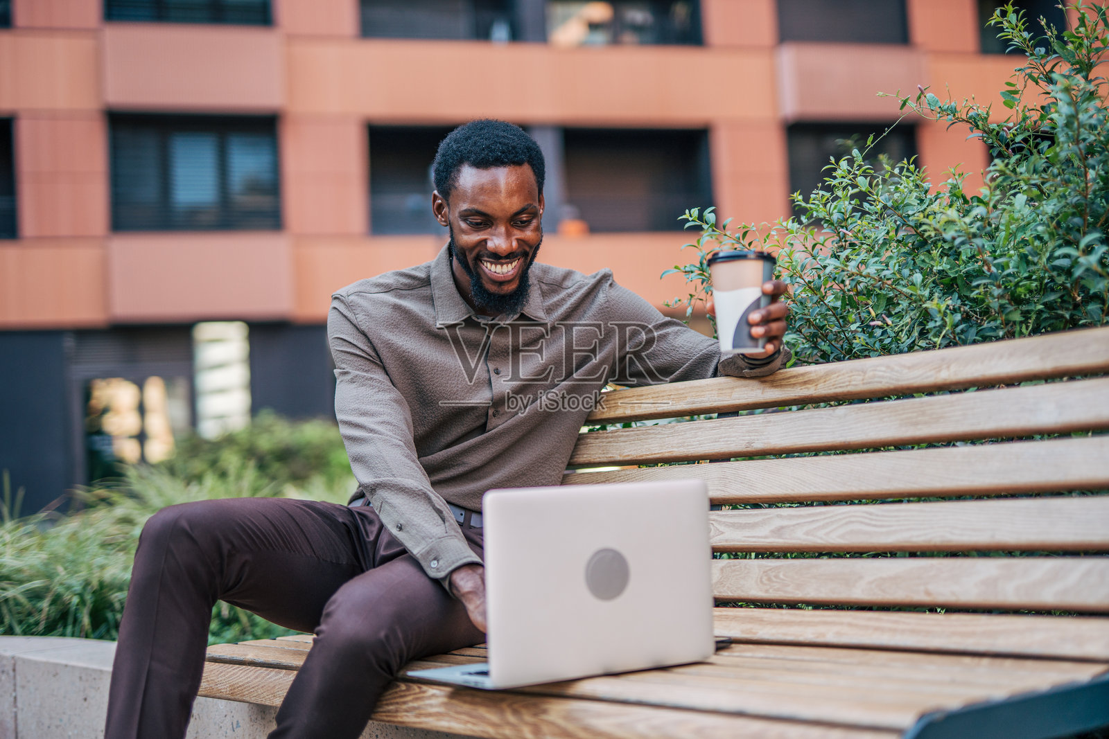 微笑的商人在户外一边享受咖啡一边使用笔记本电脑工作照片摄影图片