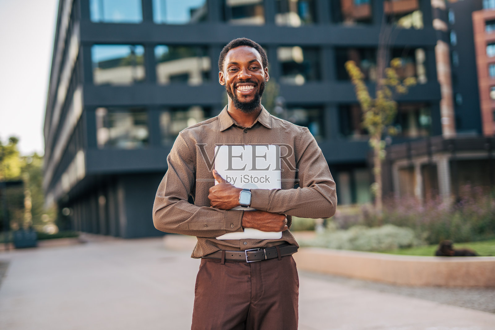 微笑的商人手持笔记本电脑站在办公楼前照片摄影图片