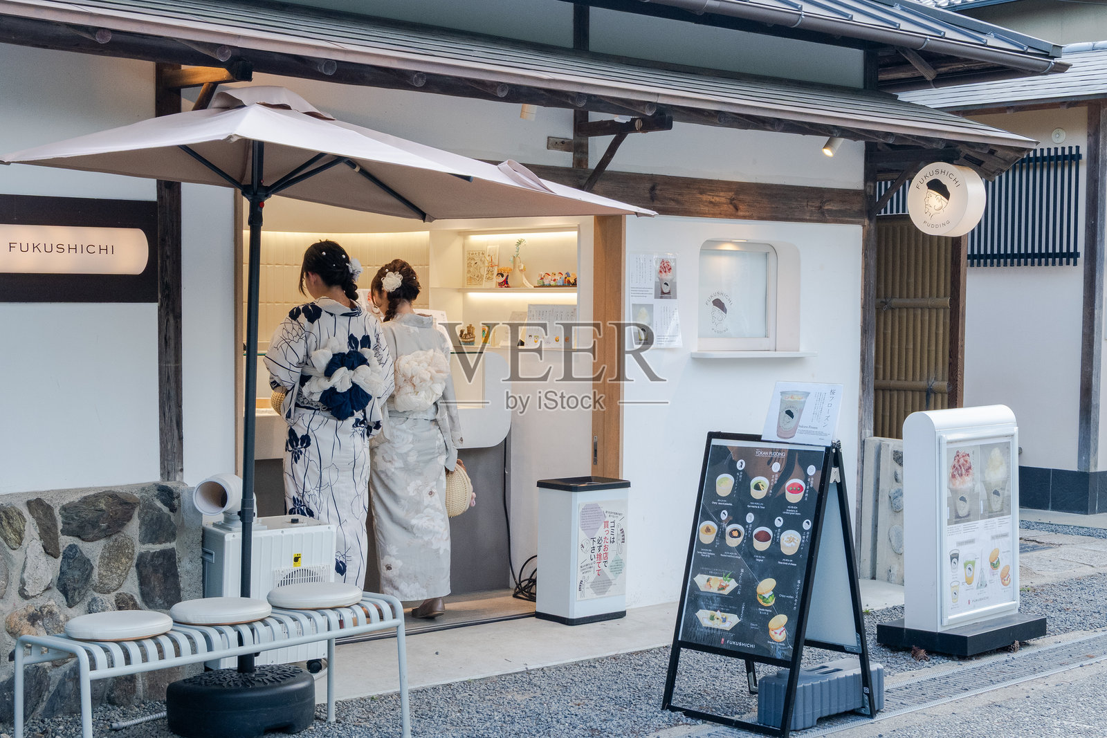 两位身着传统浴衣的女性在京都的一家甜品店前停下，展现了日本夏季文化的优雅与生动。照片摄影图片