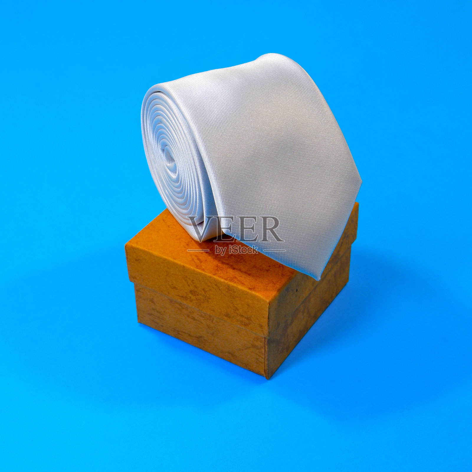 白色素色领带卷在礼品盒上，蓝色背景特写照片摄影图片