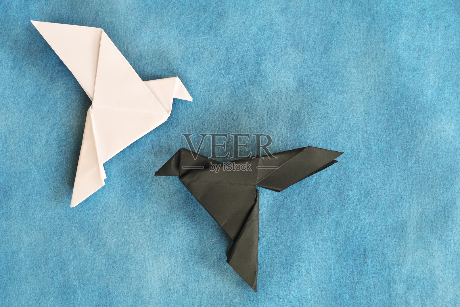 白色鸽子和黑色狂欢纸折纸在蓝色的背景。善与恶，面对恐惧和对立吸引的概念。照片摄影图片