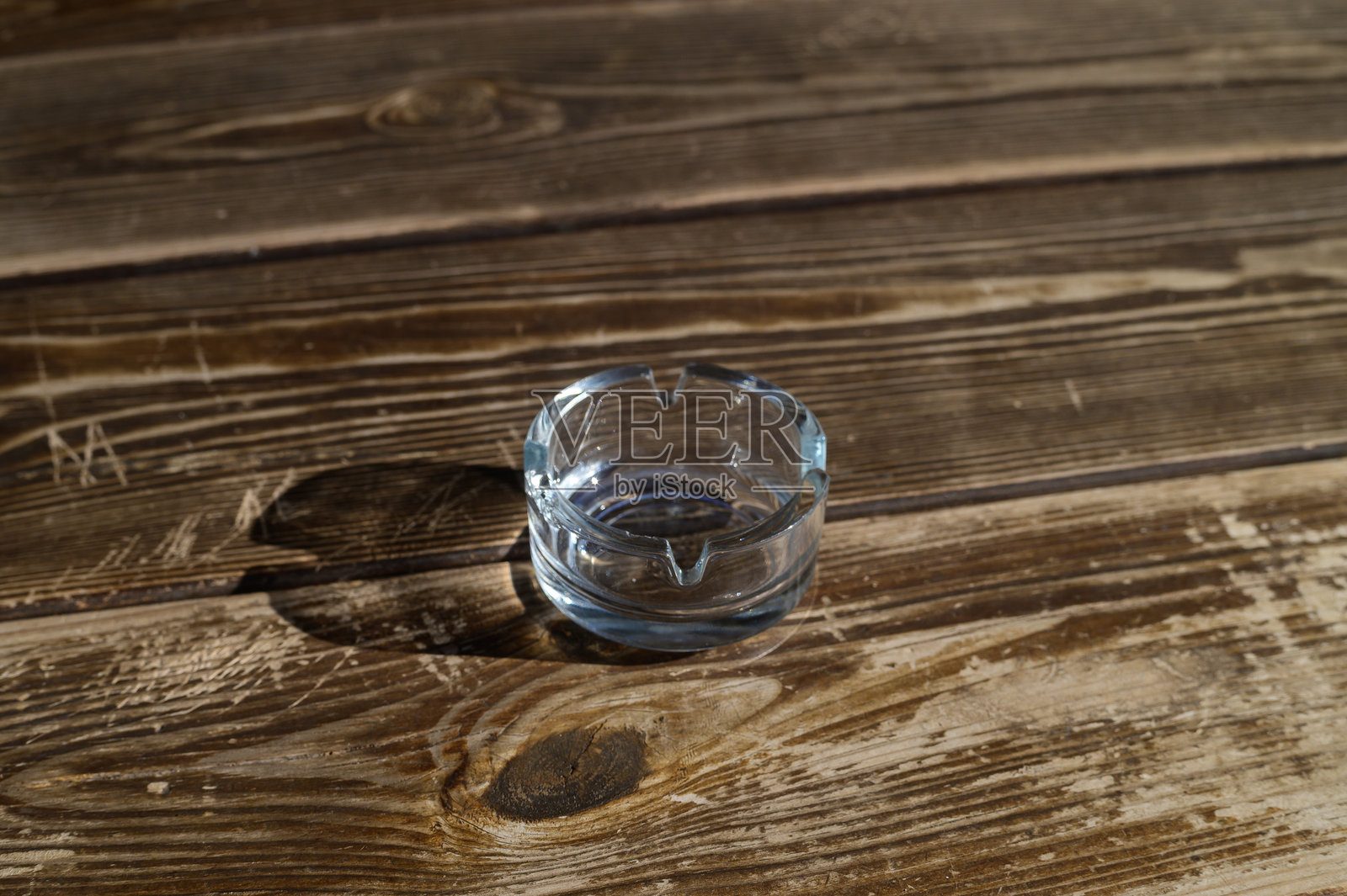 一个孤独的玻璃烟灰缸静静地放在温暖下午阳光下的风化木板上，唤起一种怀旧的感觉。照片摄影图片