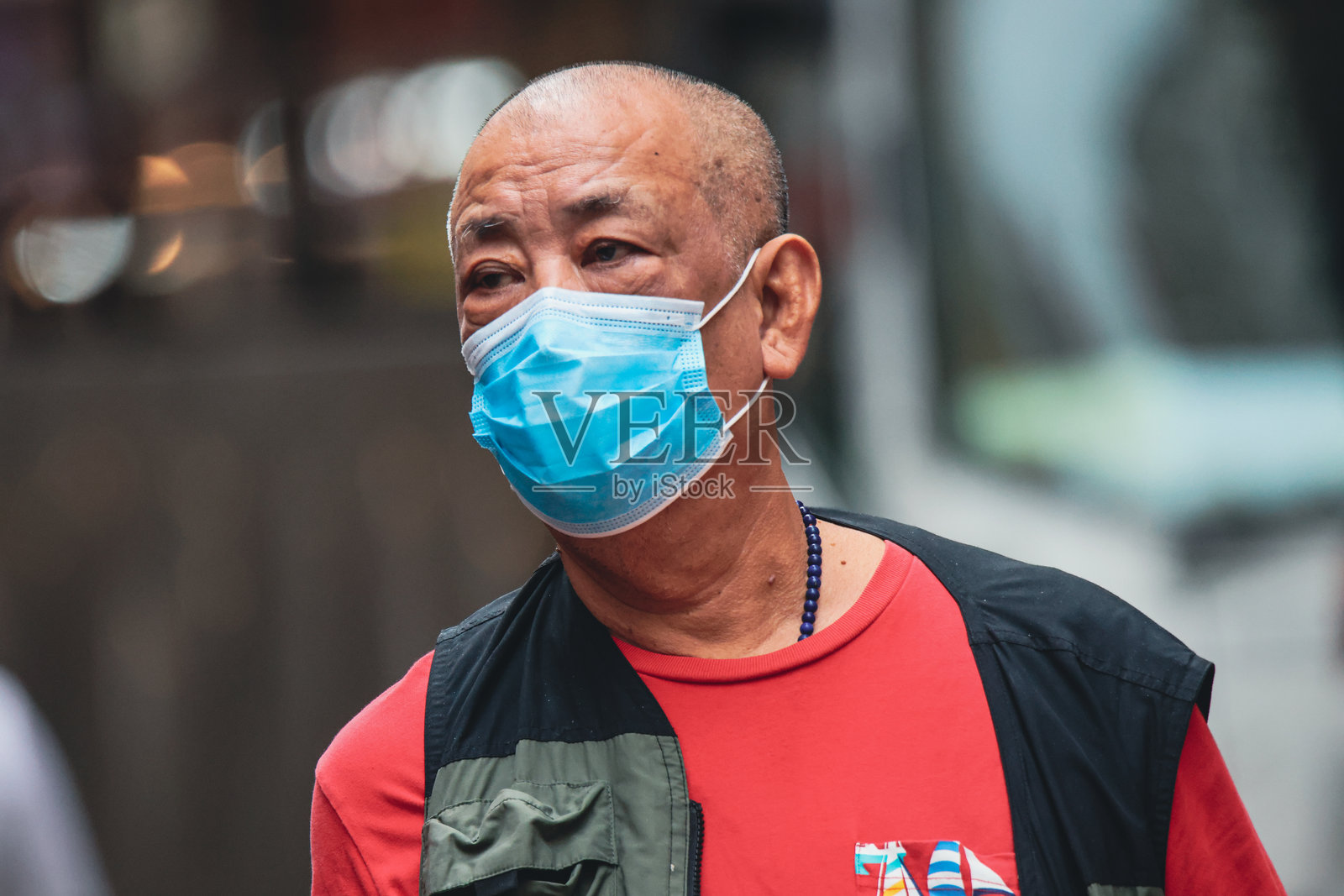 下午,一位戴着口罩的老人走过香港一条熙熙攘攘的街道照片摄影图片