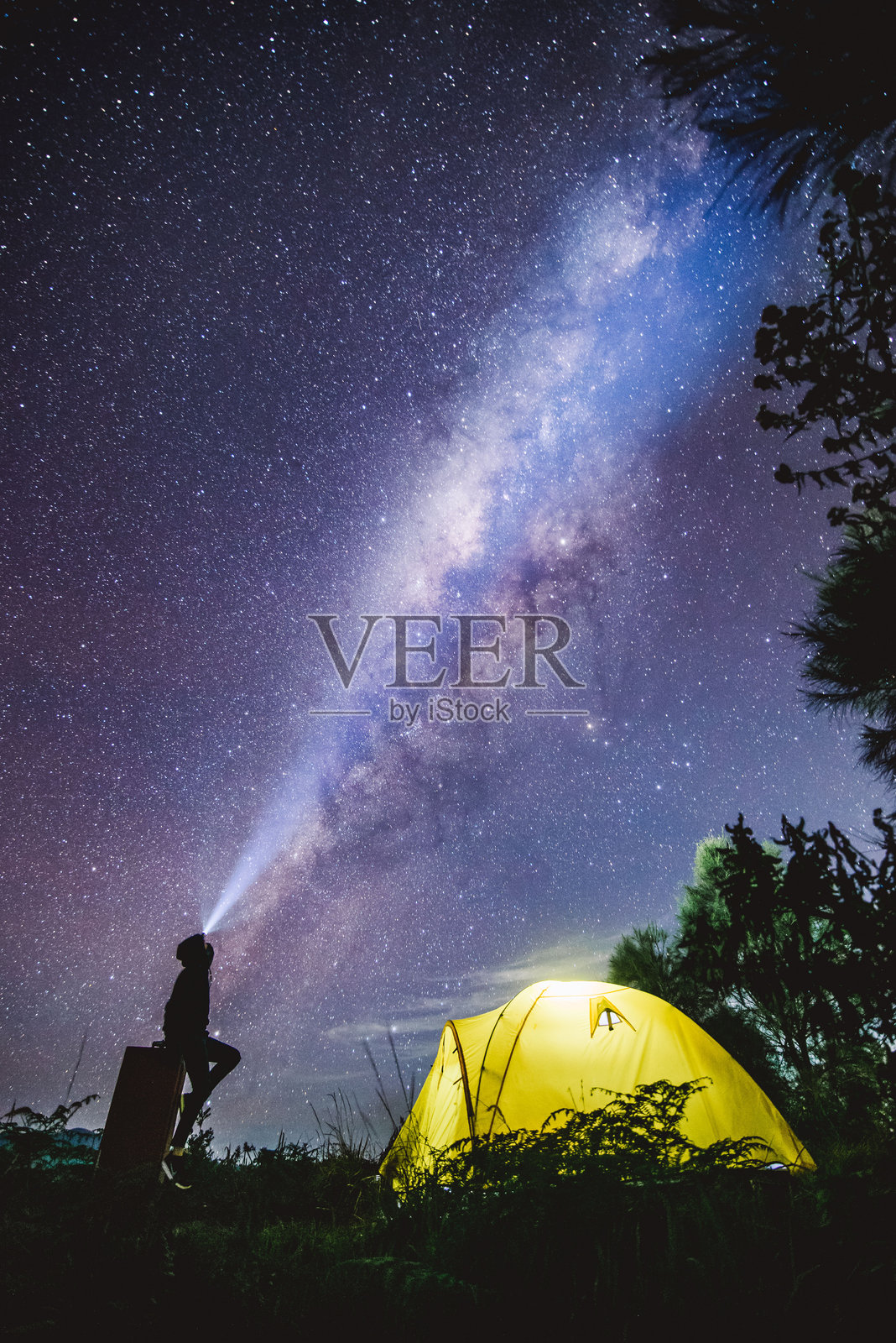 一个人在黄色帐篷里露营，头灯照向天空观察银河系。照片摄影图片