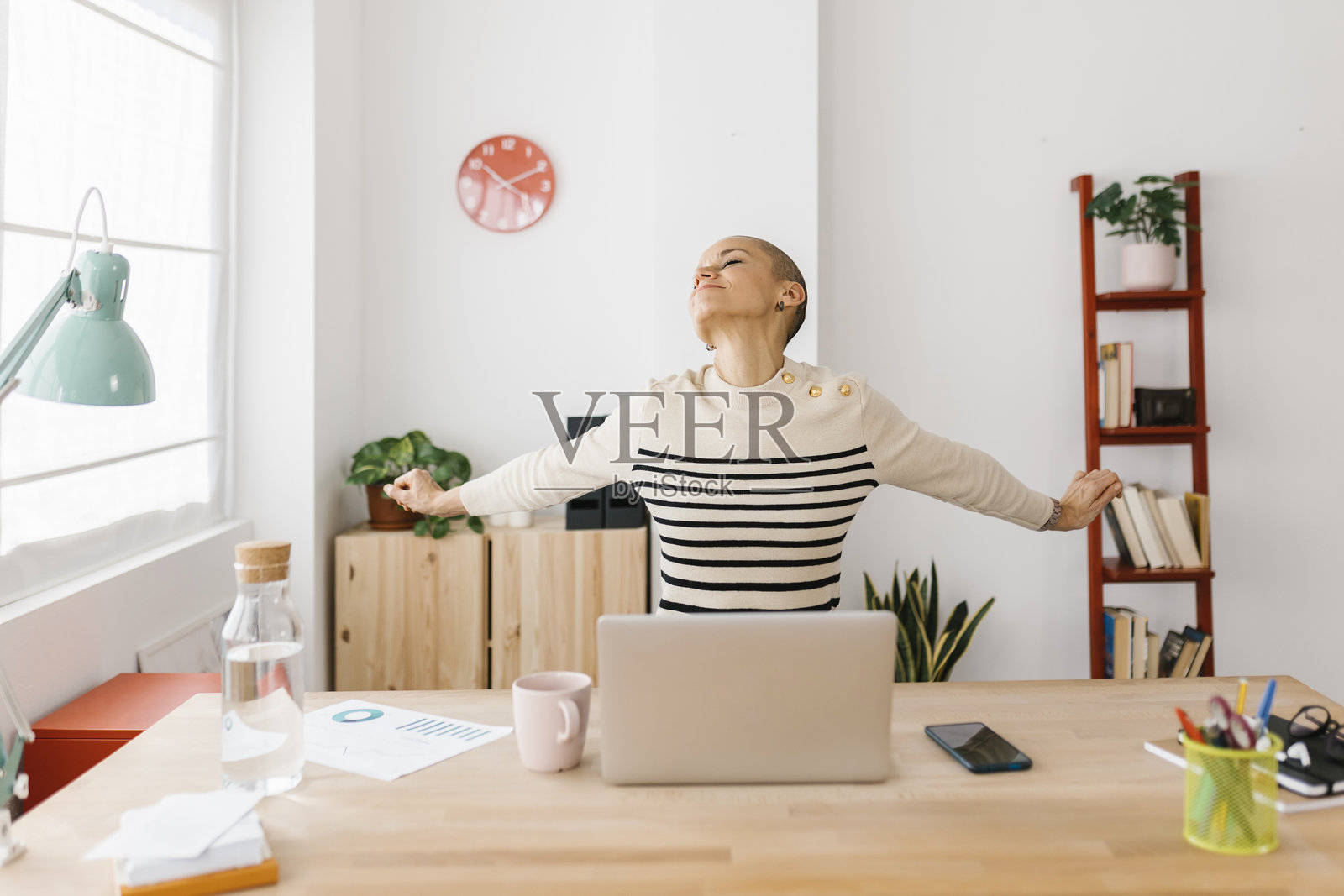微笑的中年女性在家中办公室使用笔记本电脑时伸展身体照片摄影图片