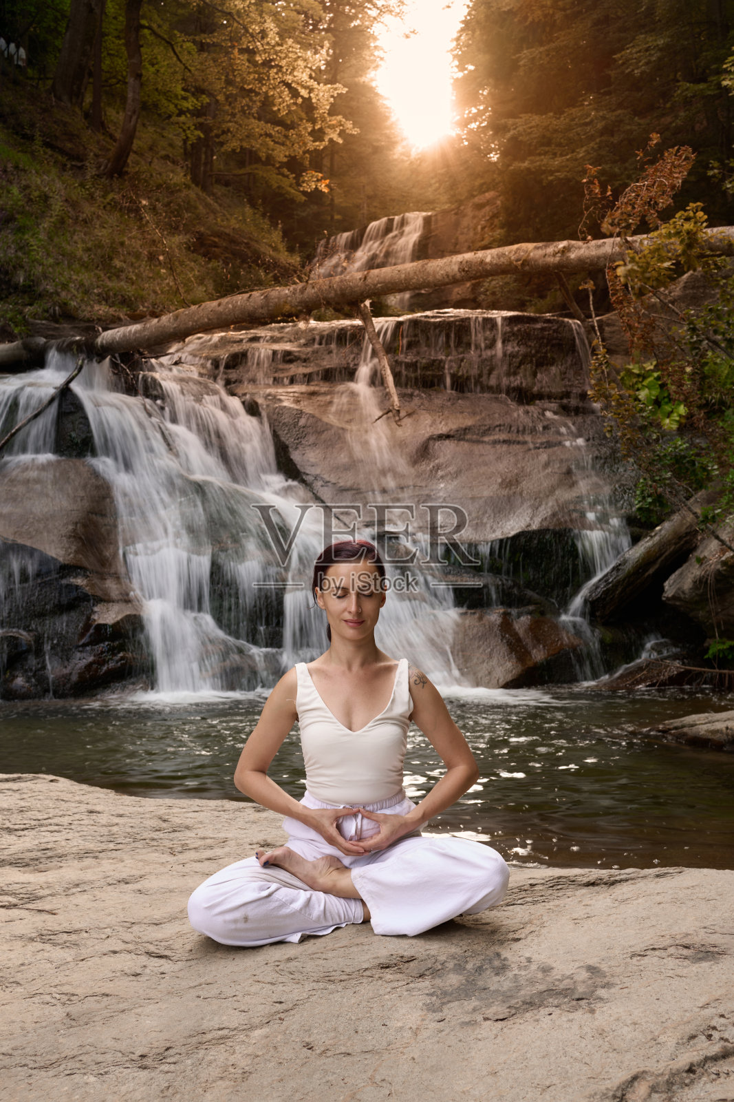 年轻女性坐在热带瀑布下的莲花坐姿中，冥想时展现出平静的力量和正念，完全与自然的能量、宁静和内心的平衡相连接。照片摄影图片