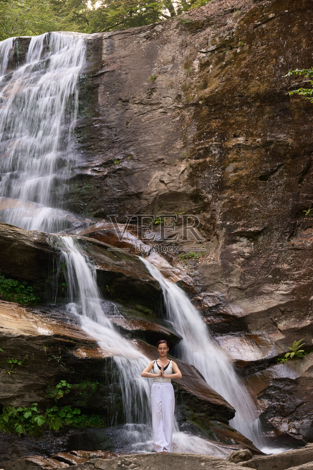 在日落时分，女人在瀑布和河流旁缓慢地练习太极，展现了自然中的和谐、平衡与健身。照片摄影图片