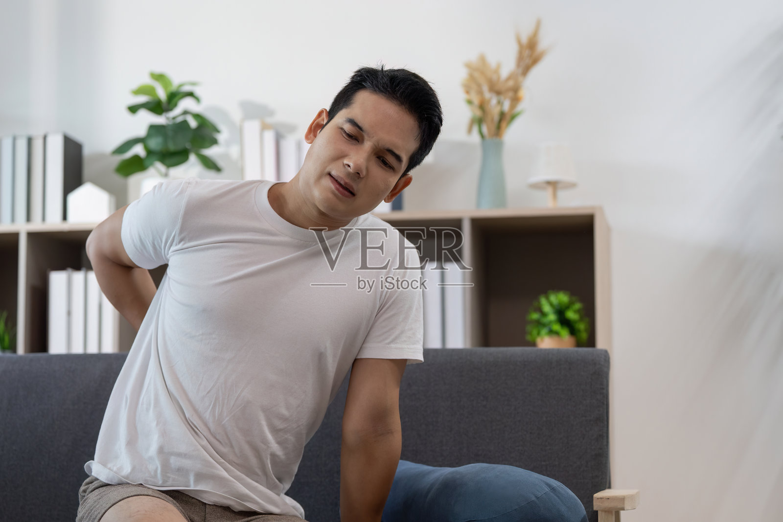 背部不适。年轻男子坐在沙发上感到疼痛。照片摄影图片