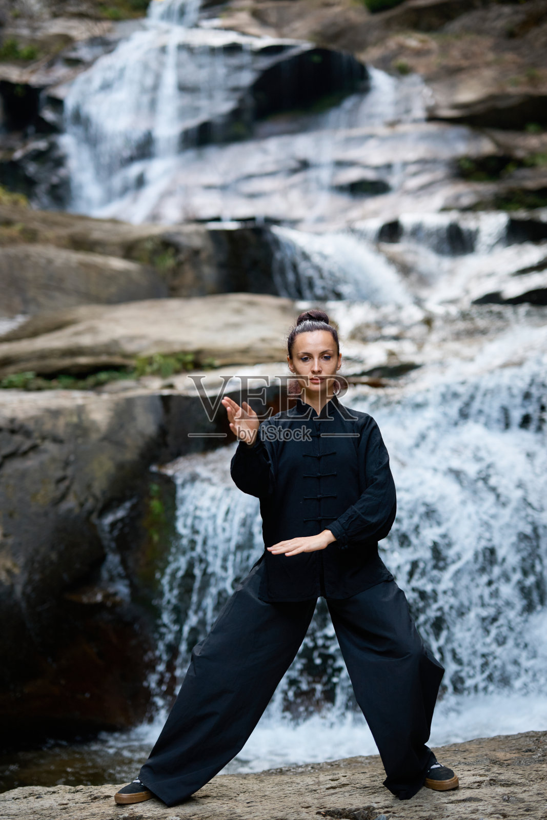 美丽的年轻女性在日落时分于瀑布和河流旁缓慢地练习太极，展现了自然中的和谐、平衡与健身。照片摄影图片