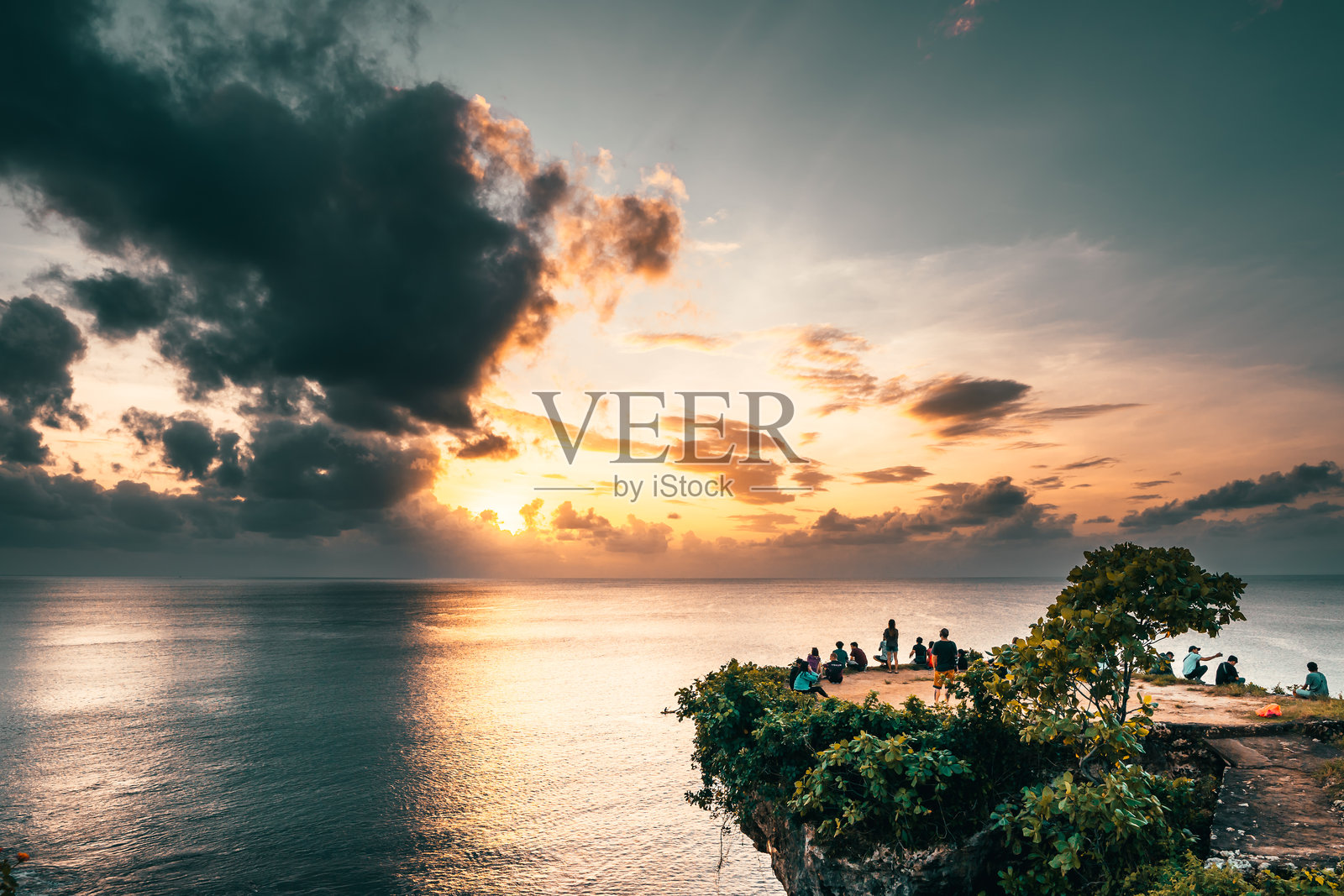 在印度尼西亚巴厘岛的热带海滩，旅行者们在山崖顶端欣赏五彩斑斓的日落。照片摄影图片