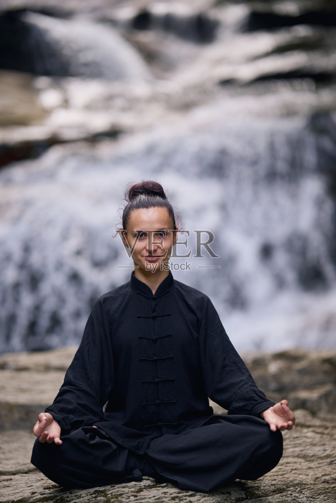 一位女性坐在莲花坐姿，正在热带瀑布下练习瑜伽和太极，冥想时展现出平静的力量和专注，完全与自然的能量、宁静和内心的平衡相连接。照片摄影图片
