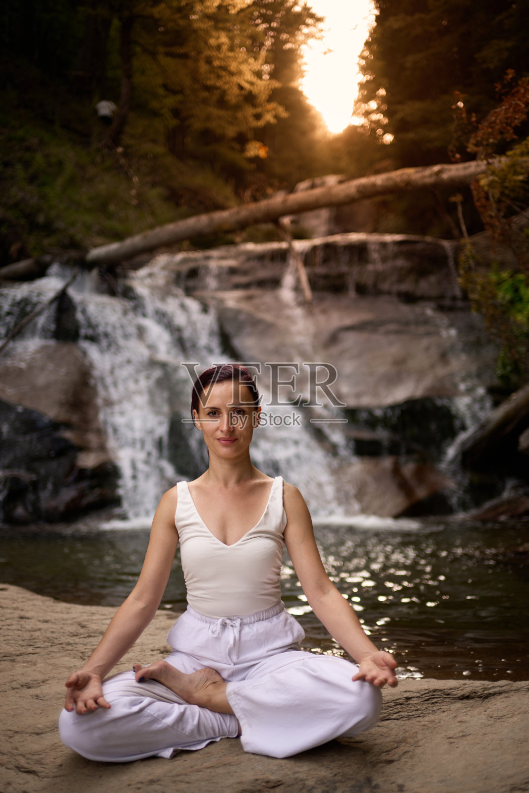 年轻女性坐在热带瀑布下的莲花坐姿中，冥想时展现出平静的力量和正念，完全与自然的能量、宁静和内心的平衡相连接。照片摄影图片