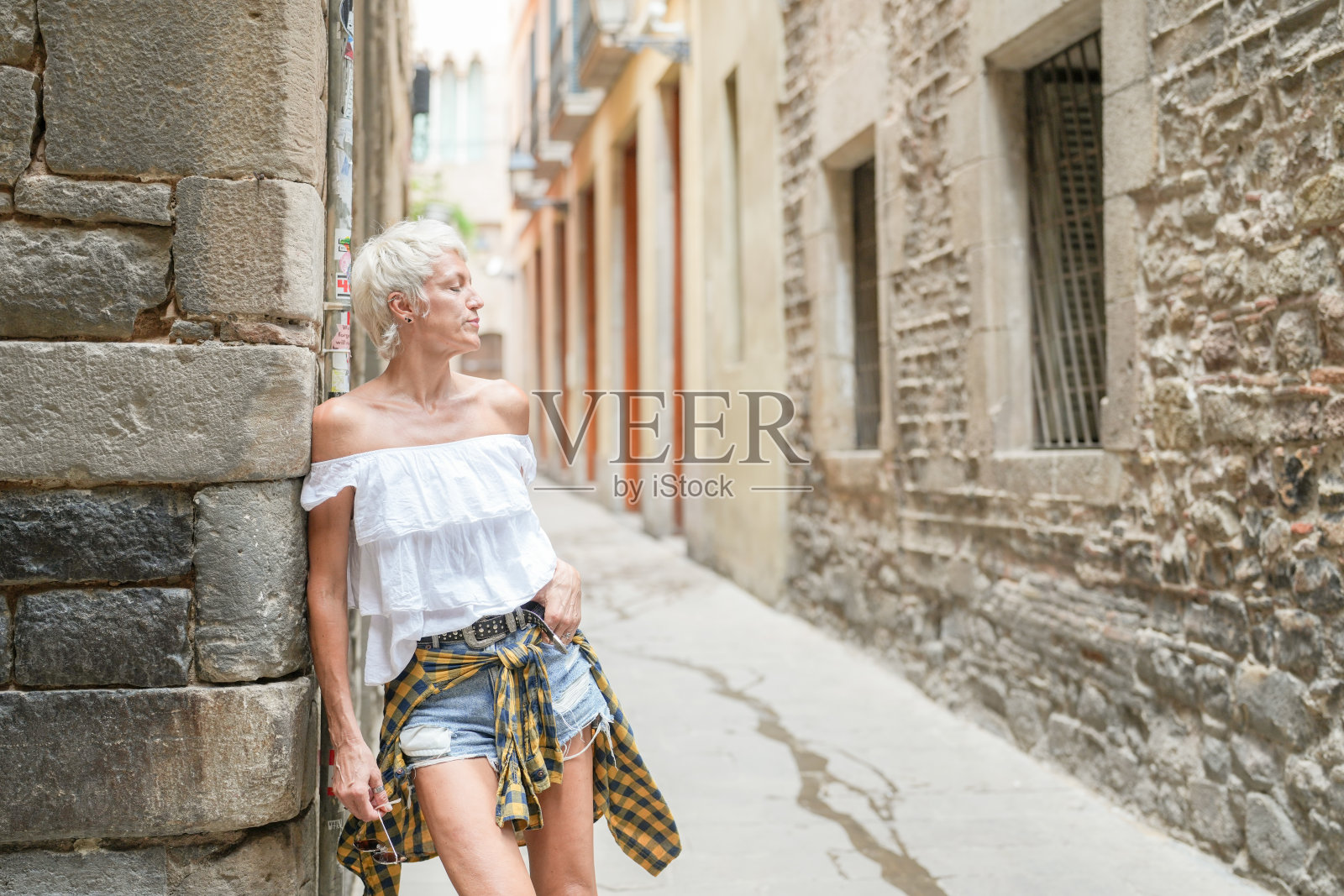 一位穿着白衬衫和蓝色短裤的女性站在砖墙上照片摄影图片