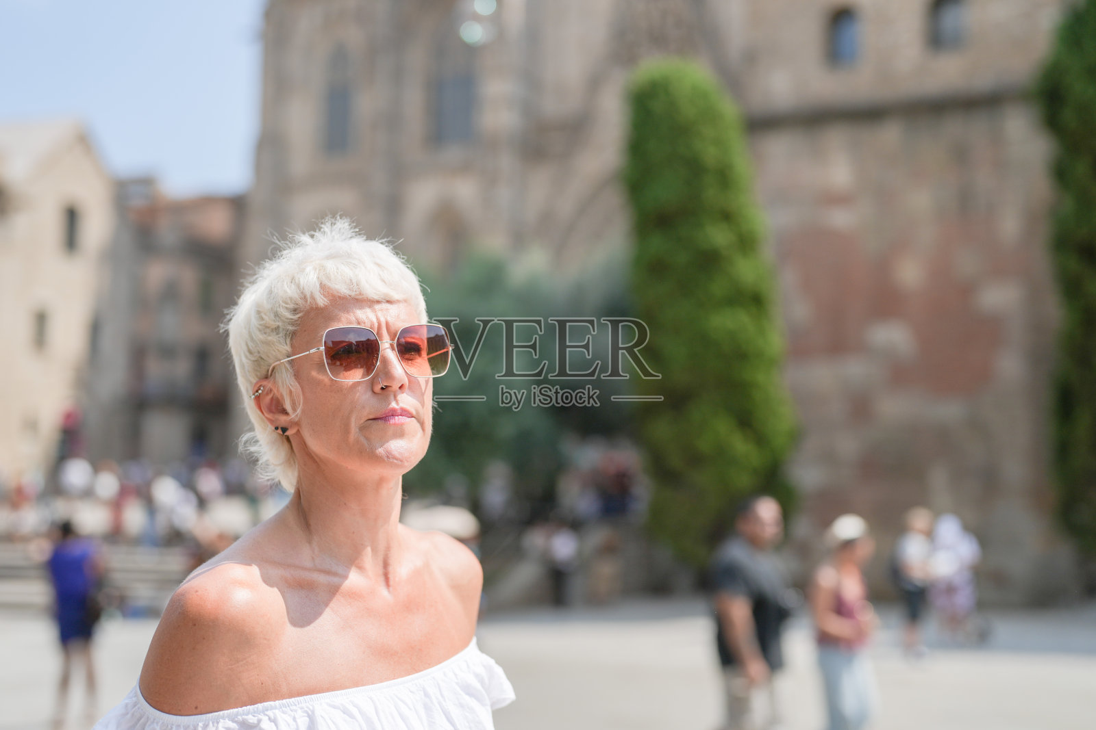 一位戴着太阳镜、穿着白衬衫的女性站在一栋建筑前。照片摄影图片