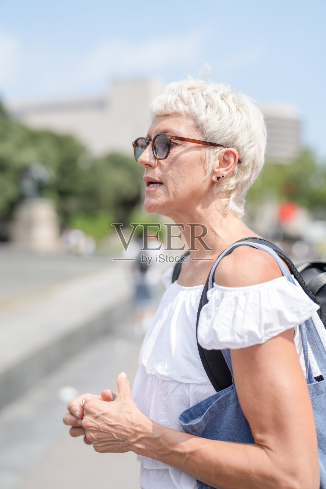 一位戴着太阳镜、穿着白衬衫的女性正在街上走。照片摄影图片