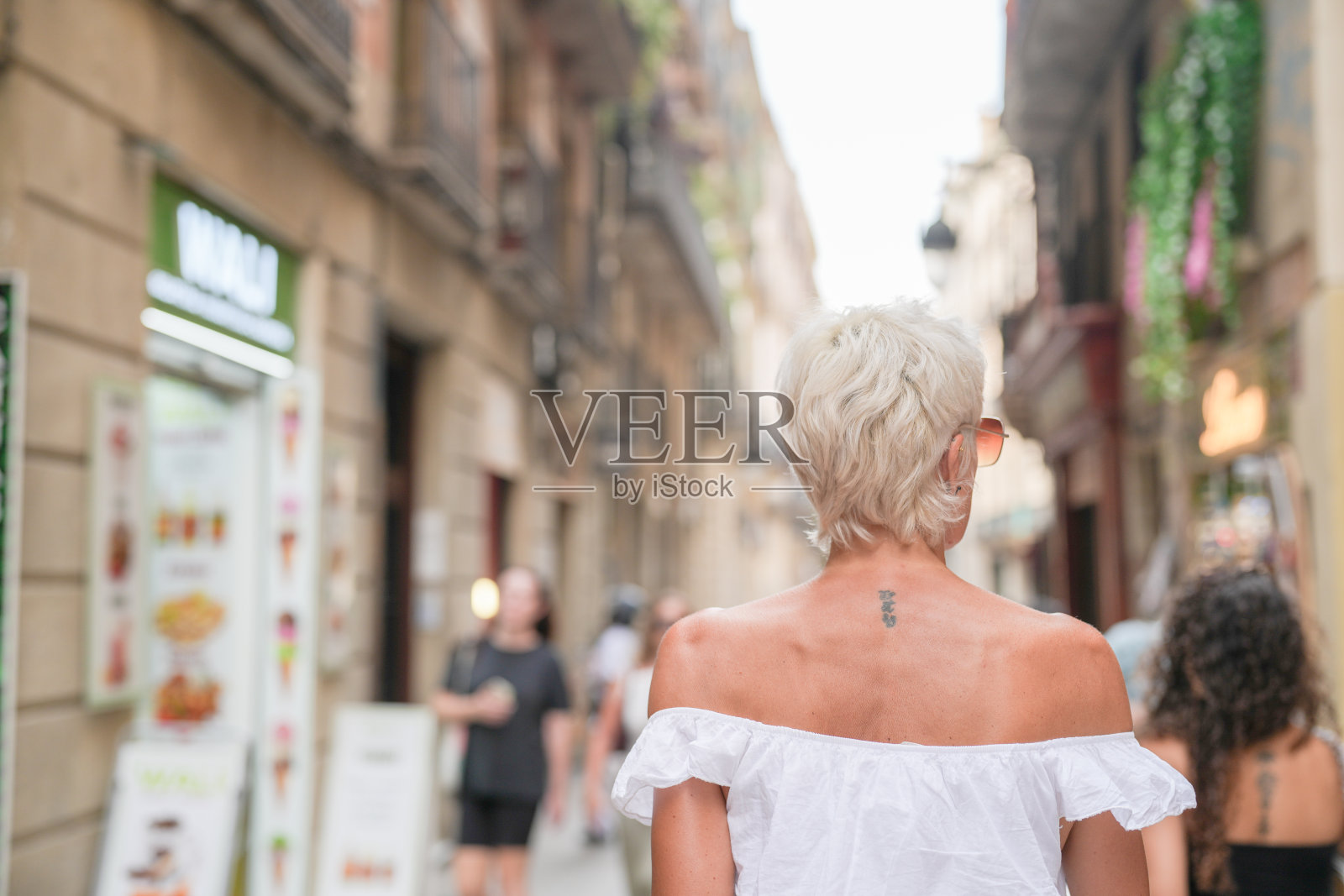 一位穿着白衬衫的女性在街上走，背上有纹身。照片摄影图片