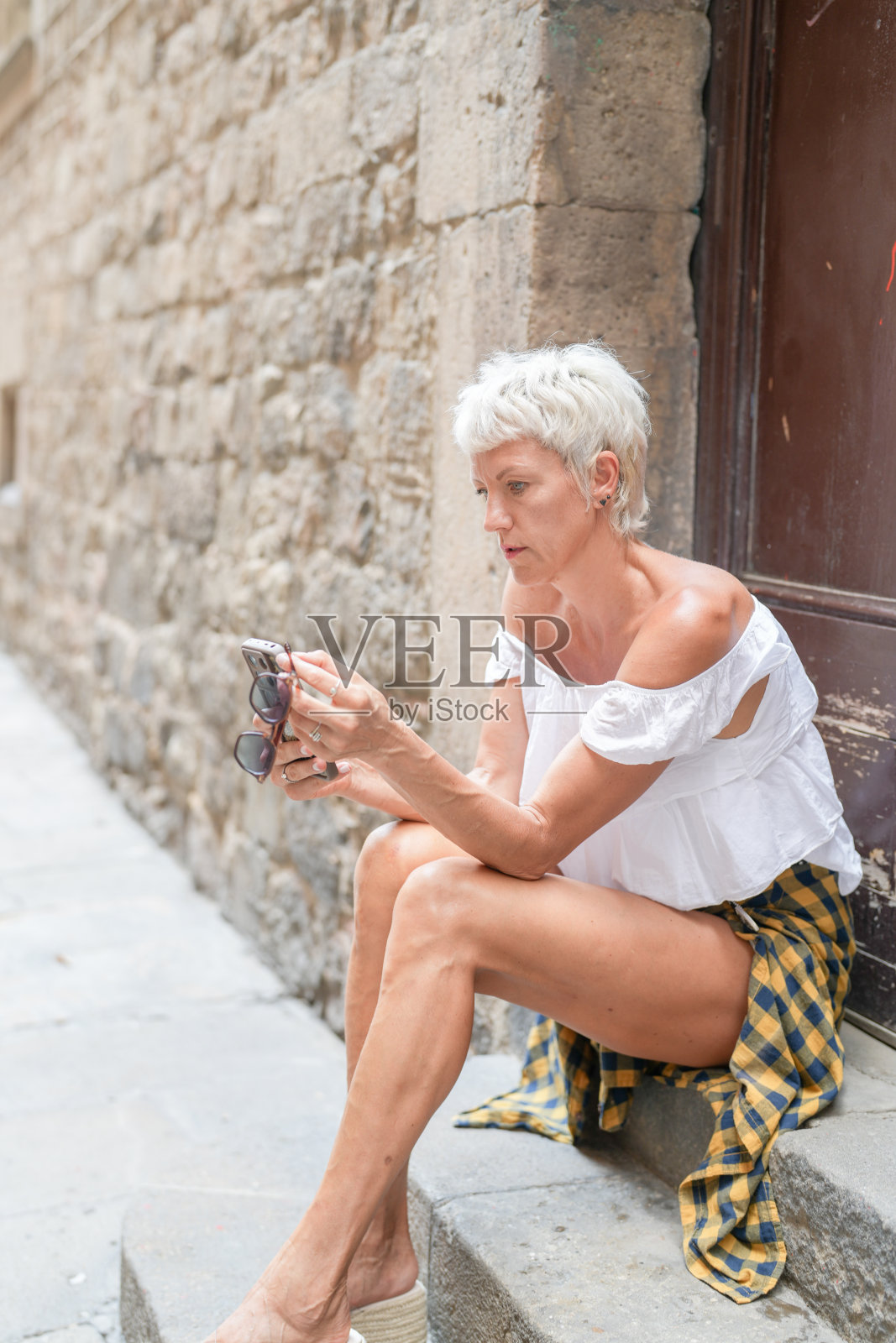 一位女性坐在台阶上，双腿交叉，手中拿着手机。照片摄影图片