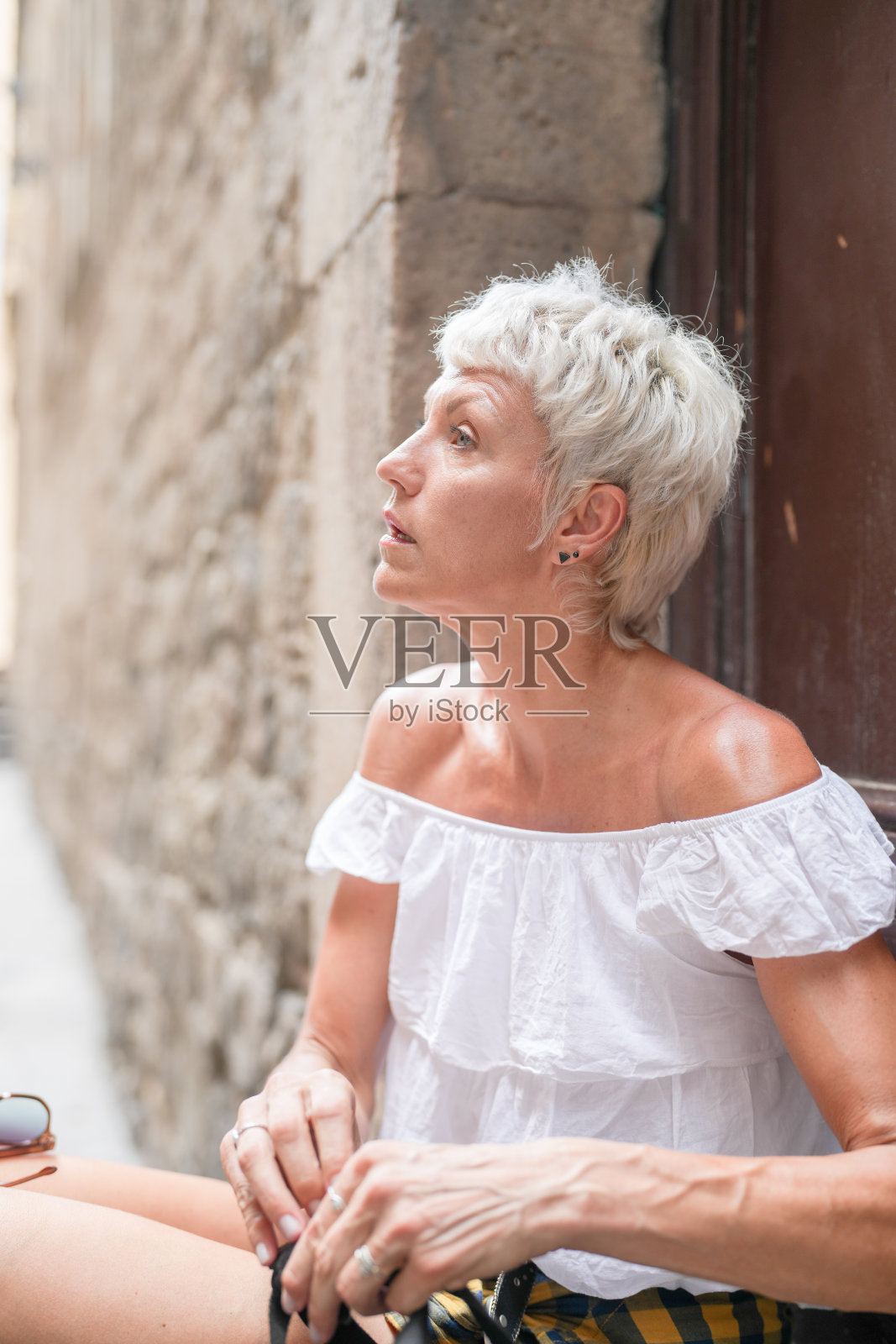 一位短发女性穿着白衬衫坐在墙上照片摄影图片