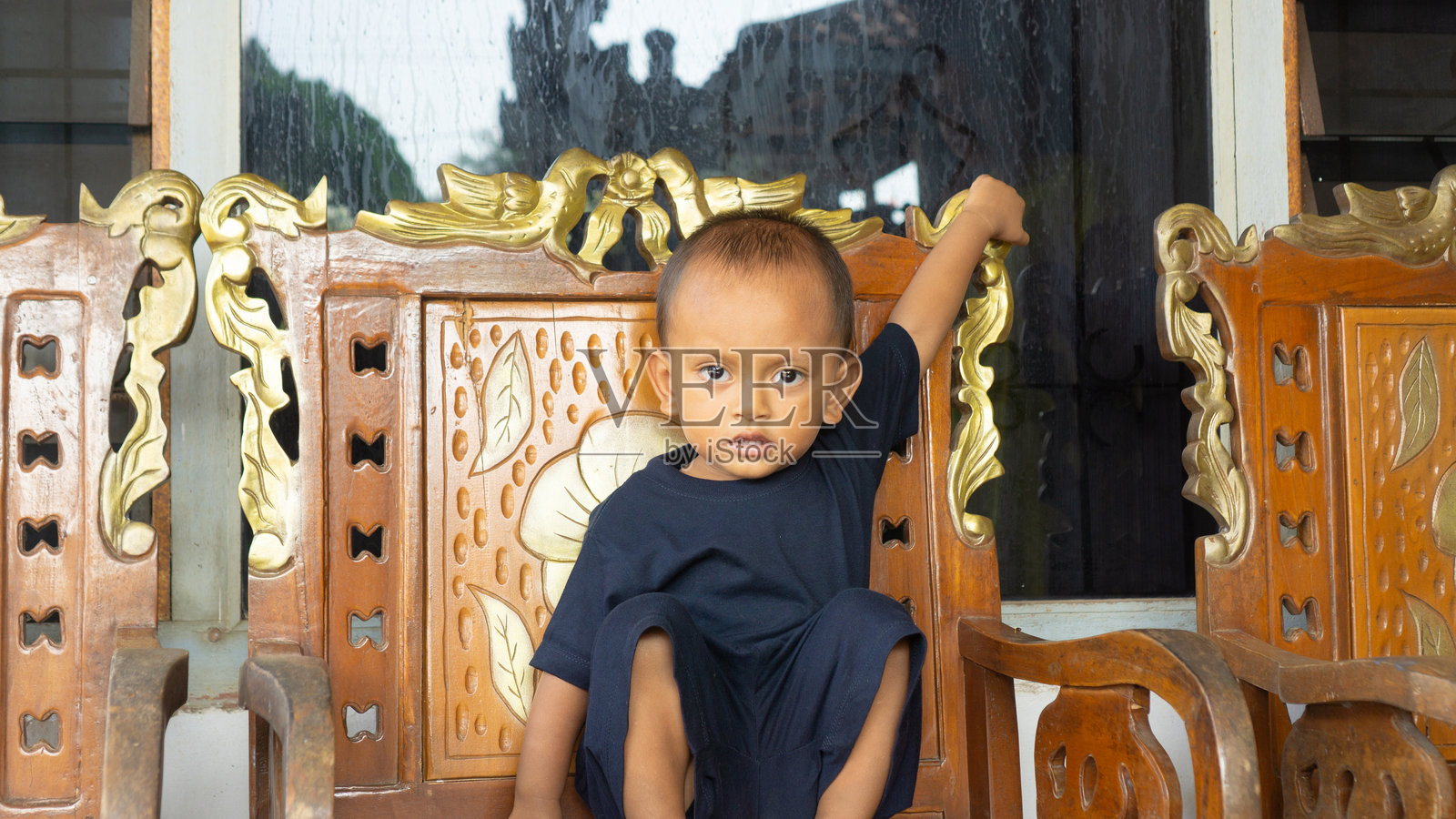 年轻男孩坐在雕刻的木椅上照片摄影图片