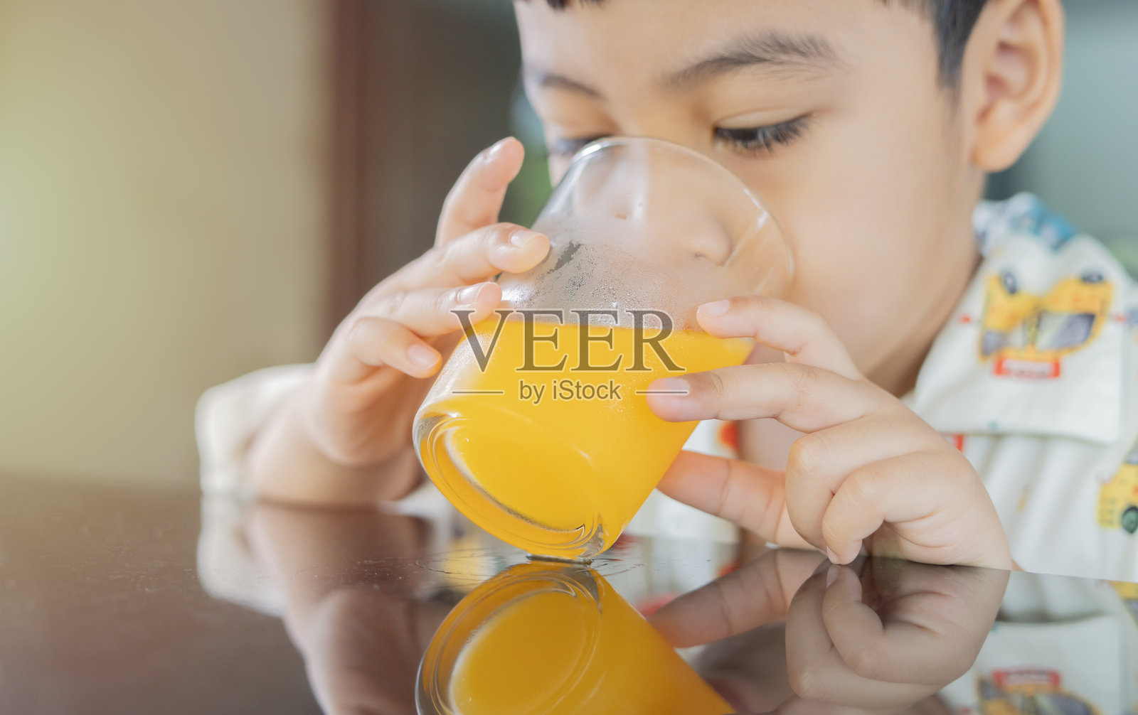 小男孩穿着睡衣，坐着喝橙汁，特写镜头。照片摄影图片