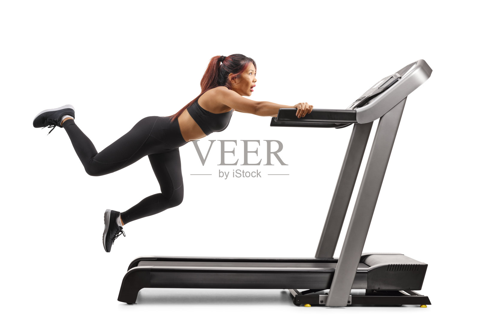 害怕的年轻女性从跑步机上摔下，双腿高高抬起。照片摄影图片