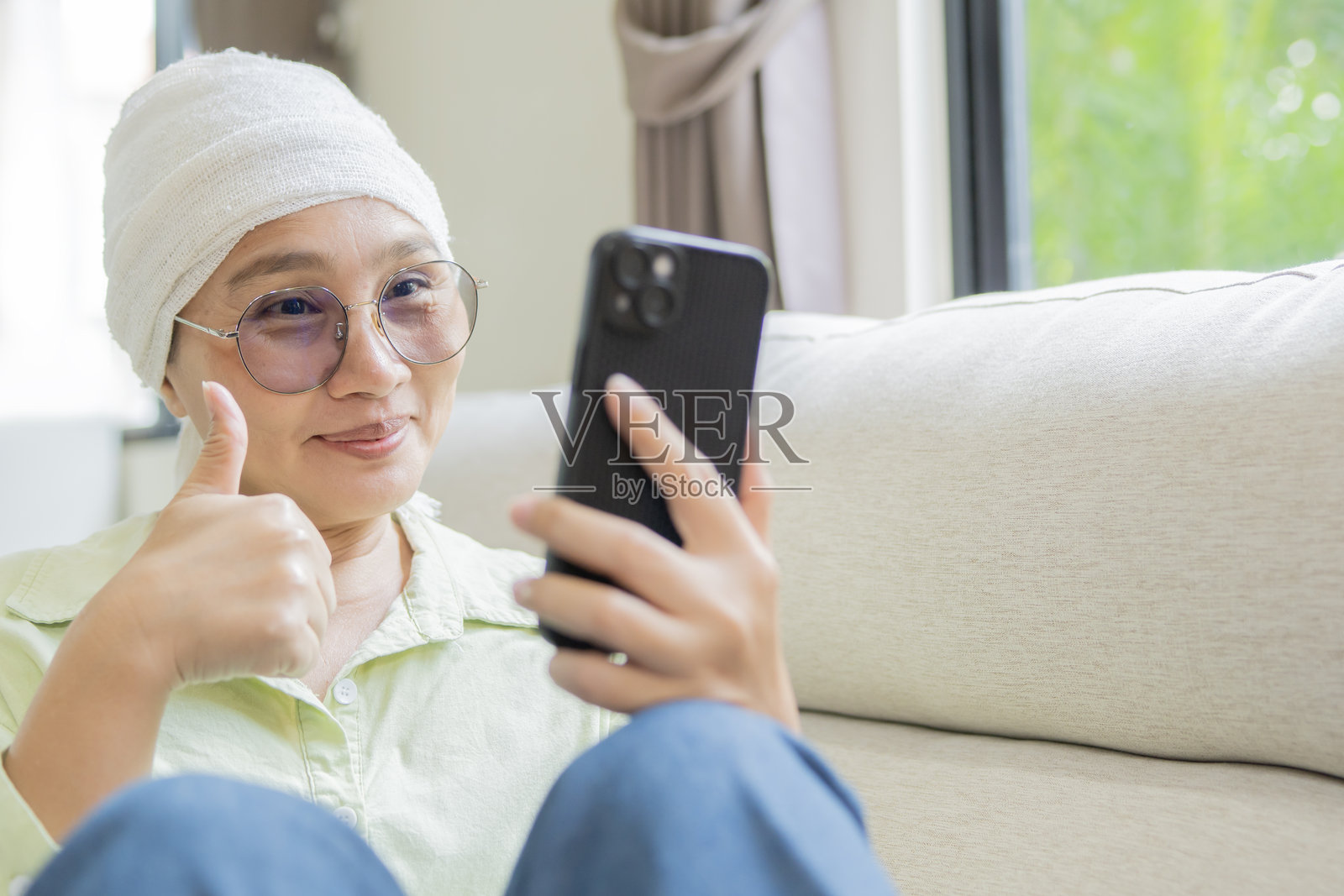 快乐的成熟亚洲女性在化疗后戴着眼镜，正在用手机通话照片摄影图片